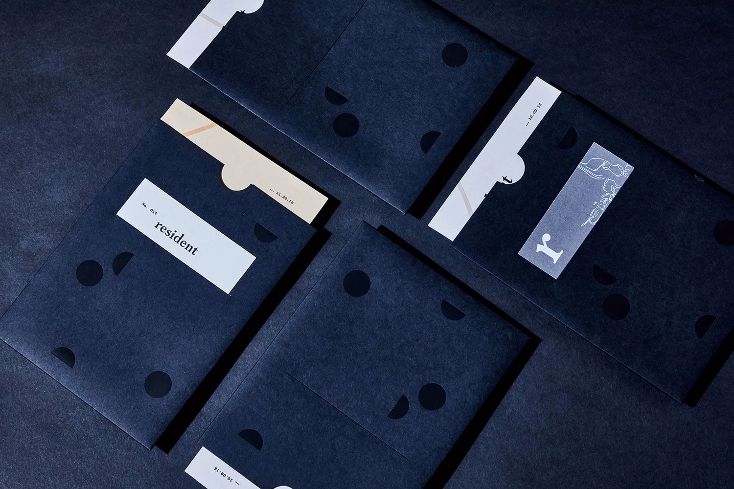 Four dark envelopes with abstract shapes and text elements, arranged on a black surface.