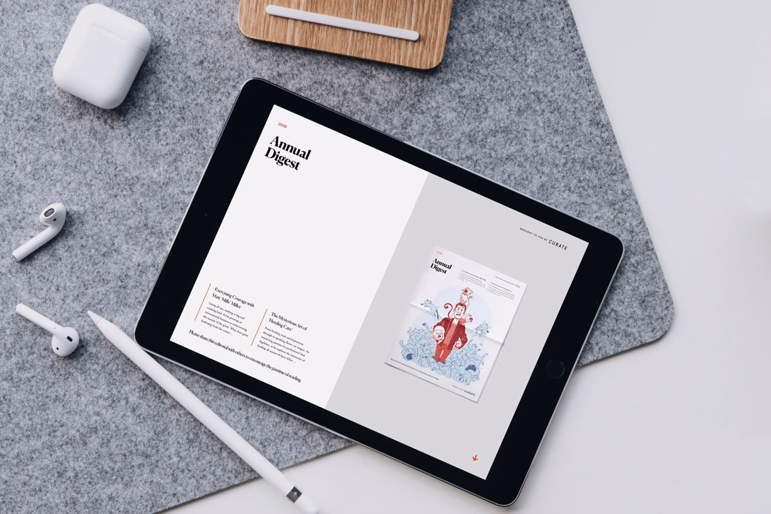 An iPad displays an open annual digest with colorful illustrations, surrounded by AirPods and a white pencil on a felt surface.