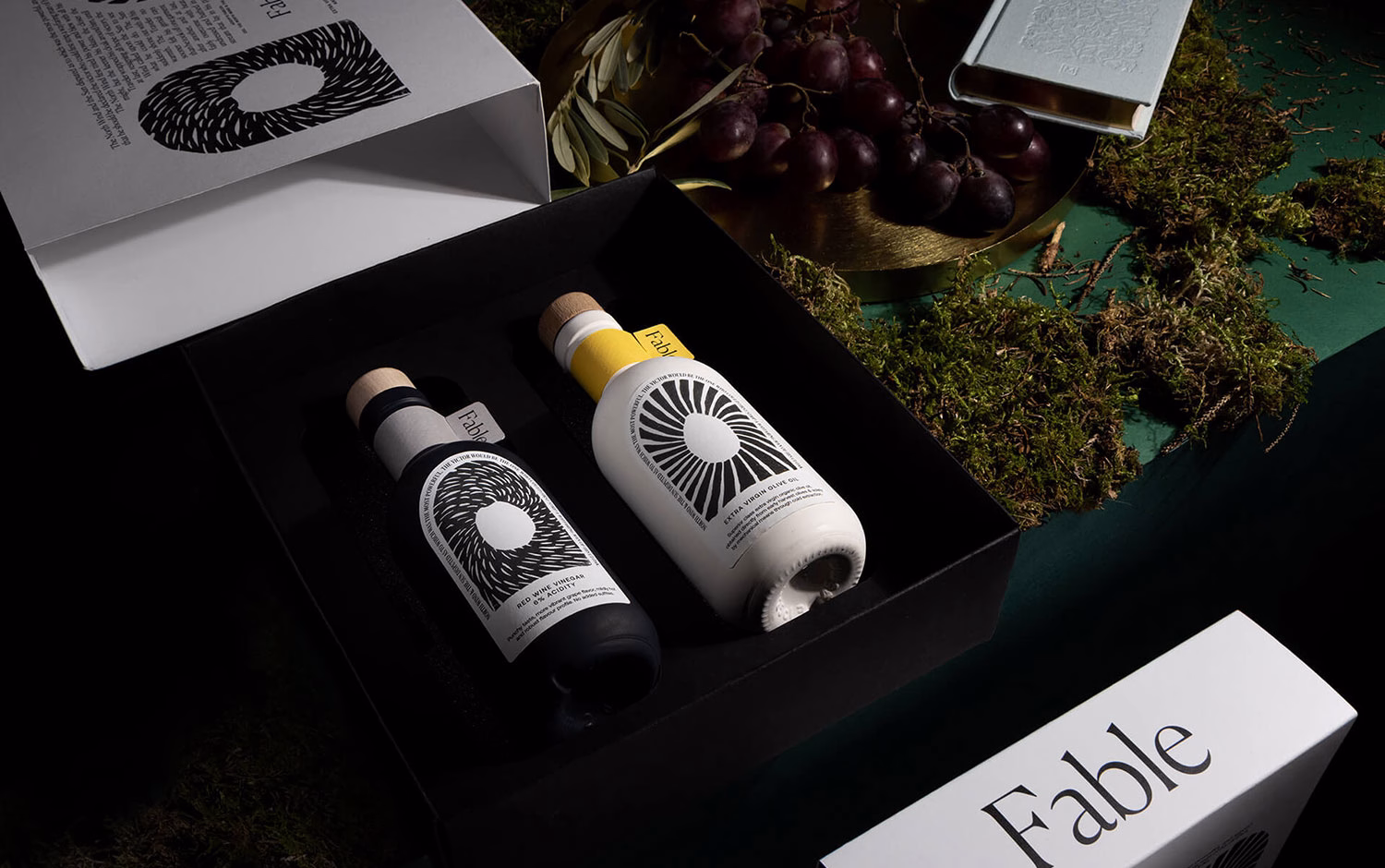 A black box contains two bottles, one white and one black, each with striking circular patterns and wooden caps.