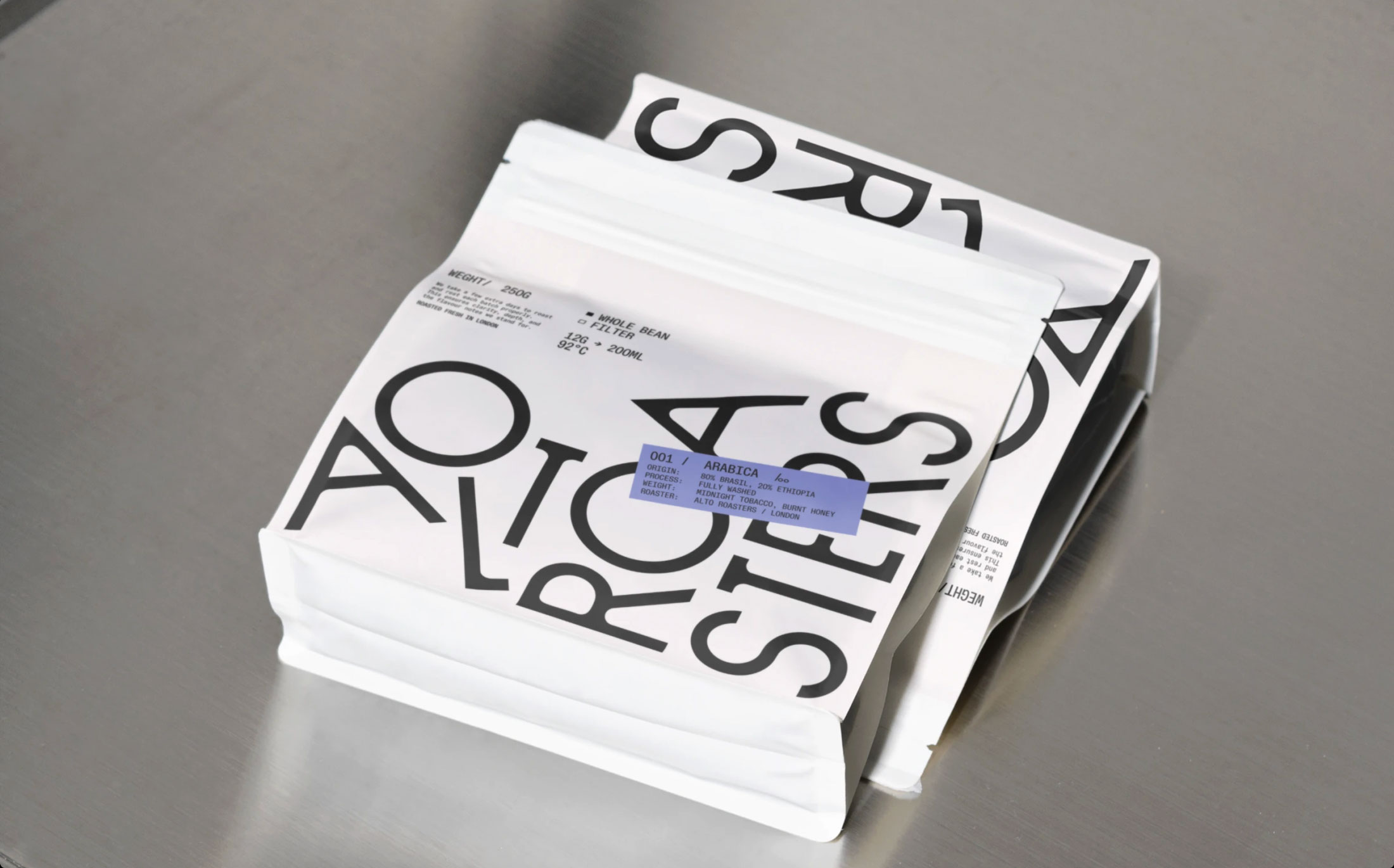 Two white coffee bags with bold black text and a lavender label on a gray surface.