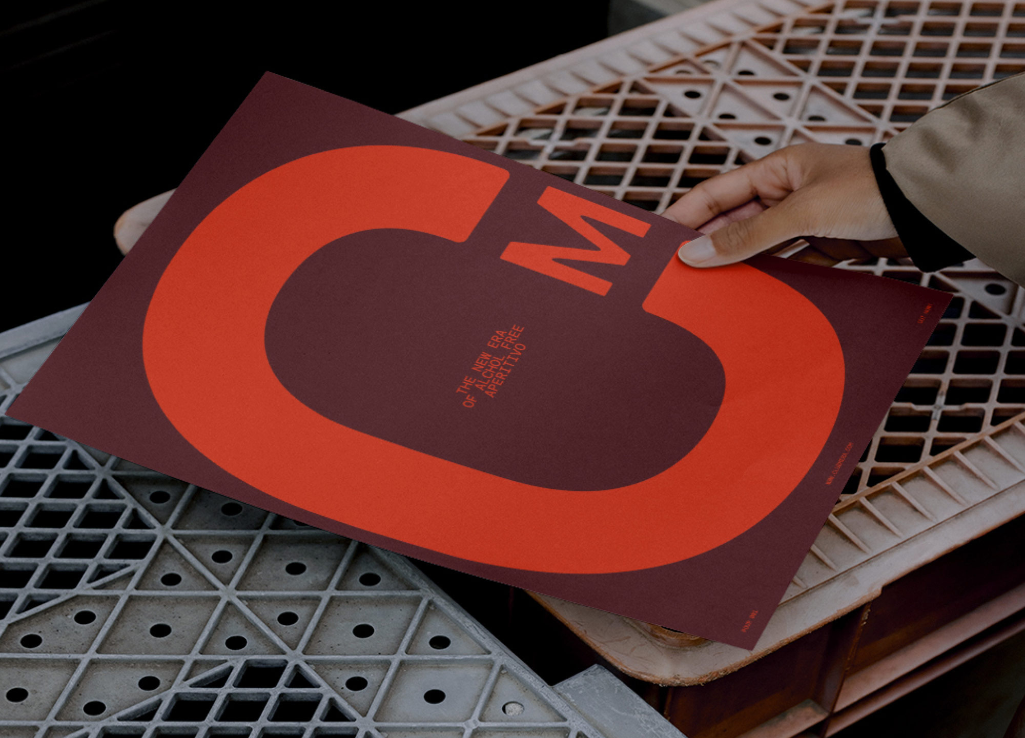 Hand holding a red and brown poster with bold letters C and M on a lattice surface.