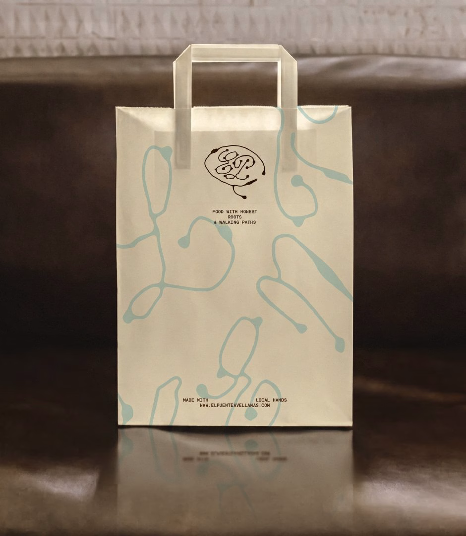 A cream-colored bag features flowing blue lines and the El Puente logo, reflecting the restaurant's beach identity.