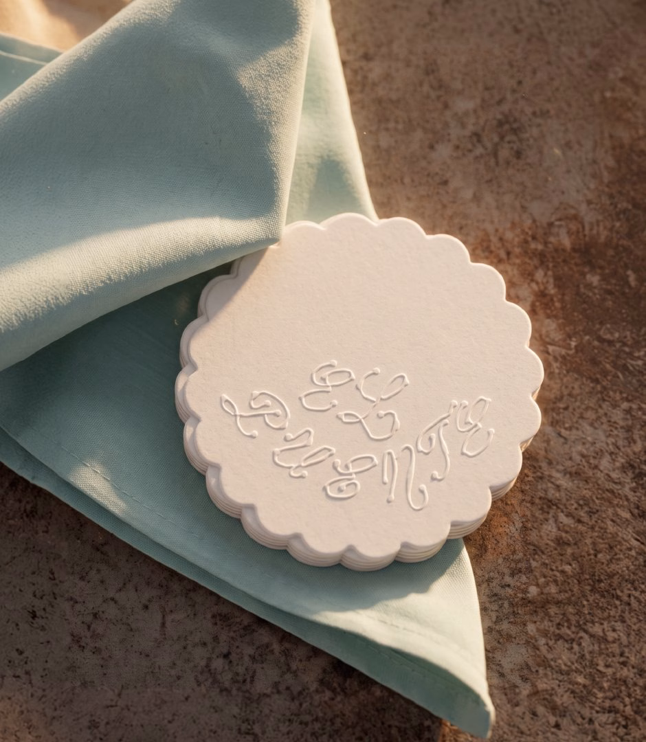 A textured white coaster featuring "El Puente" lettering rests on a light blue napkin against a sandy surface.