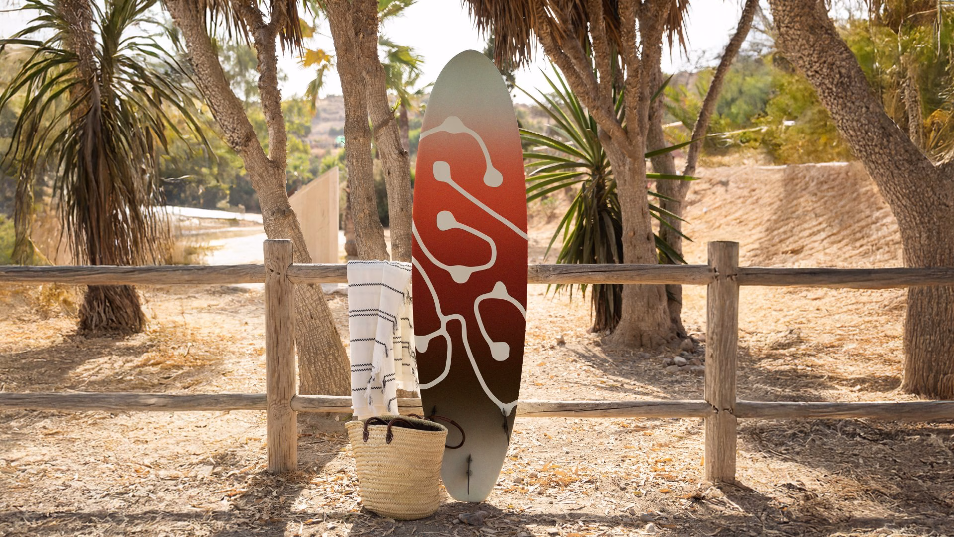 A surfboard with a gradient of earthy tones features a white snail trail design, embodying El Puente's brand identity.