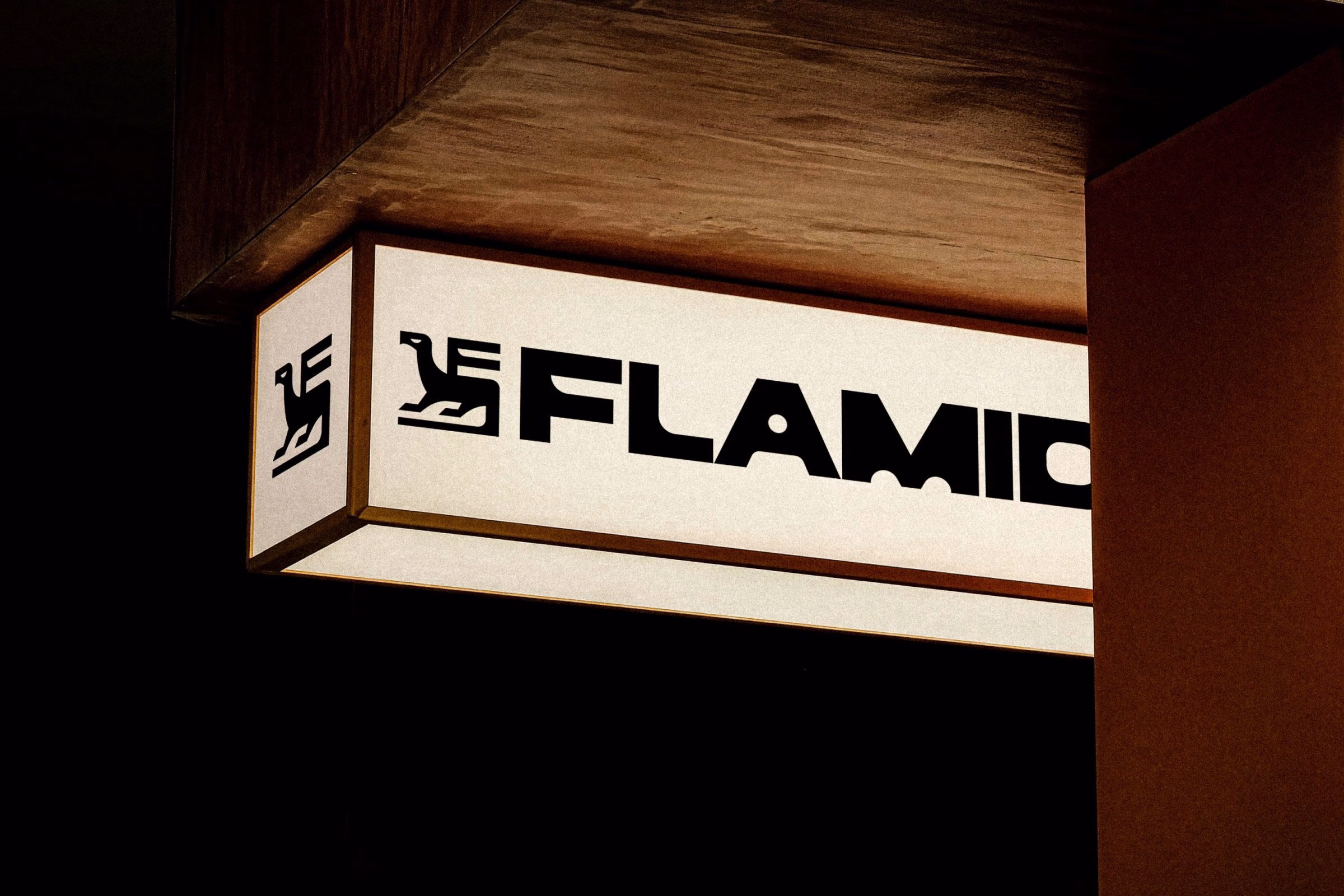 Flamid's logo featuring a bird-in-the-F symbol, displayed on an illuminated sign with a warm wood frame.