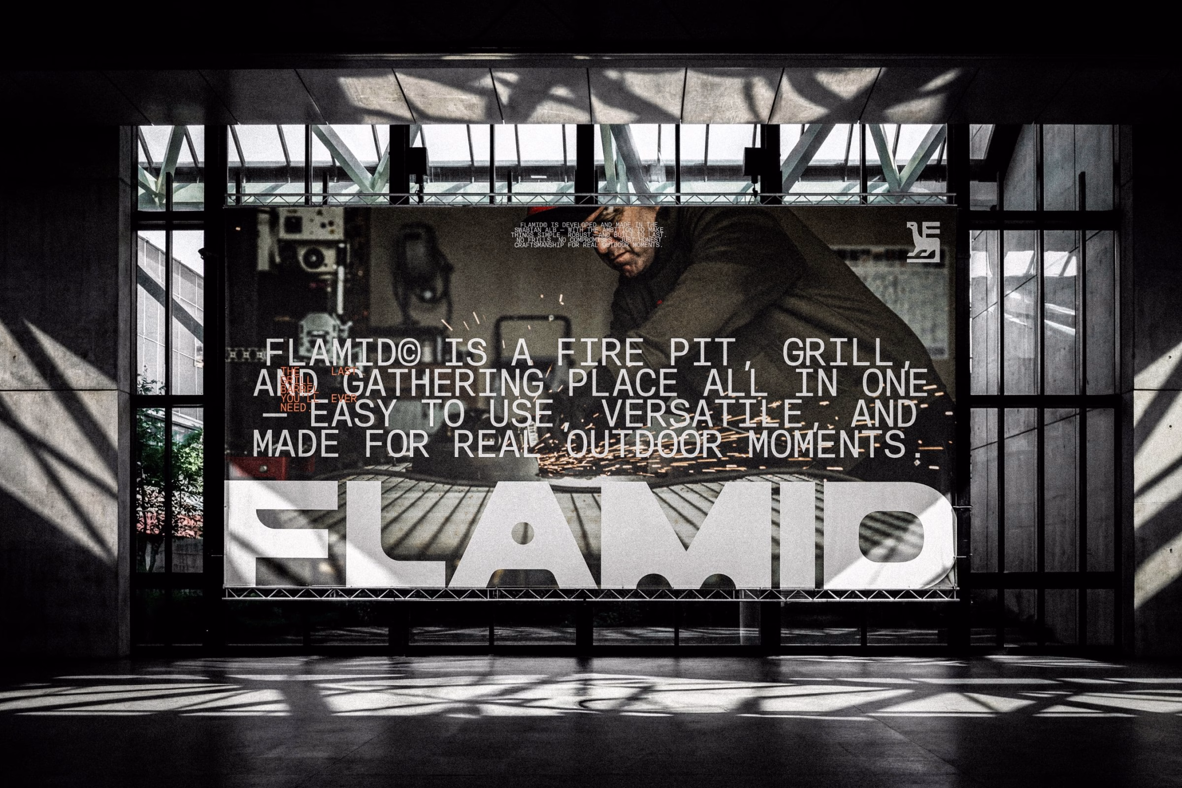A large, bold white lettering spelling "FLAMID" sits against a backdrop of a person working with steel and sparks.