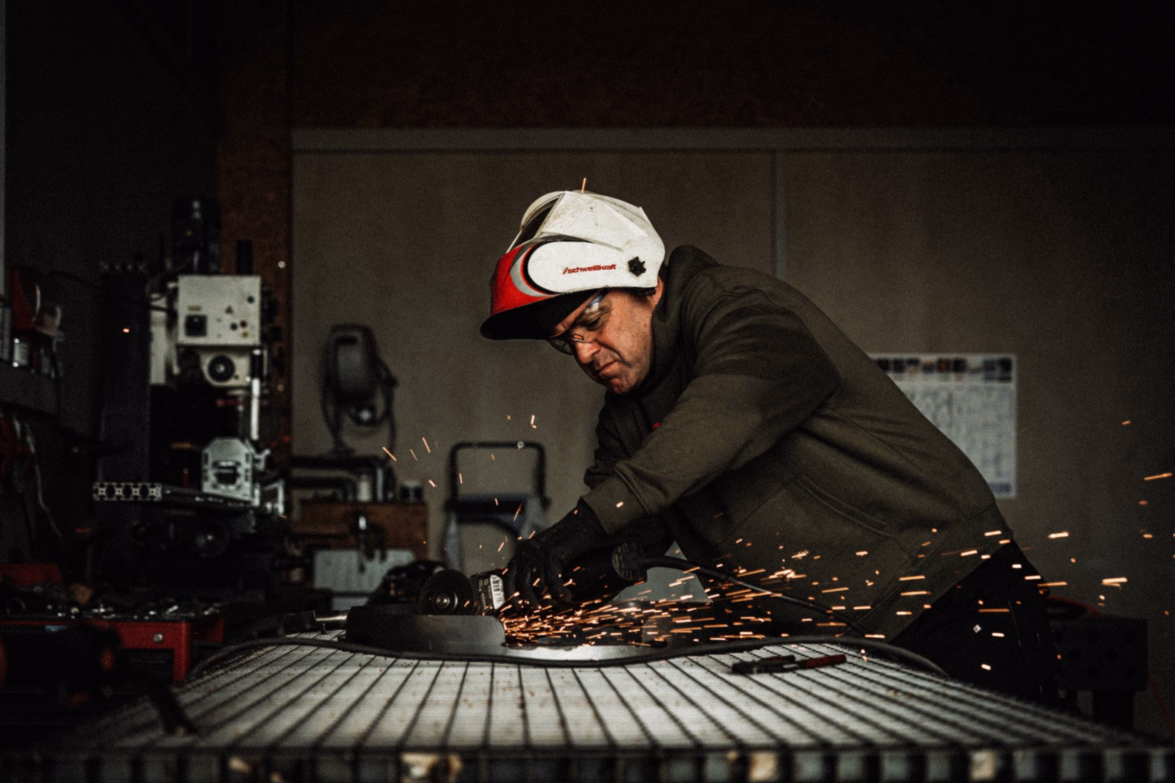 A craftsman grinds metal, generating sparks in a workshop, emphasizing the artisanal process behind Flamid's steel grills.