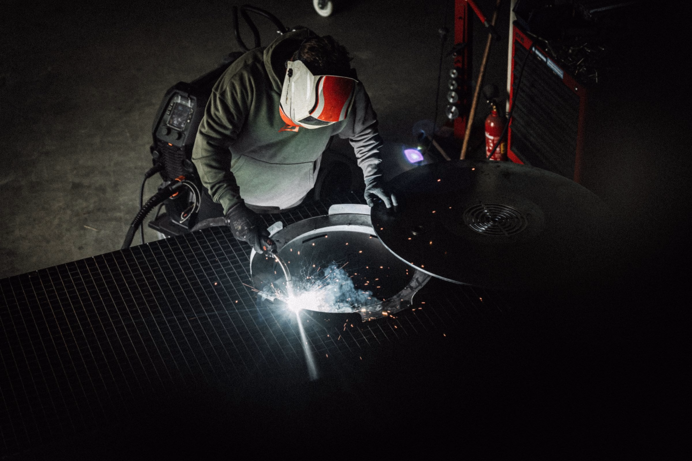 A welder creates sparks while working on a steel grill, highlighting craftsmanship in Flamid's branding project.