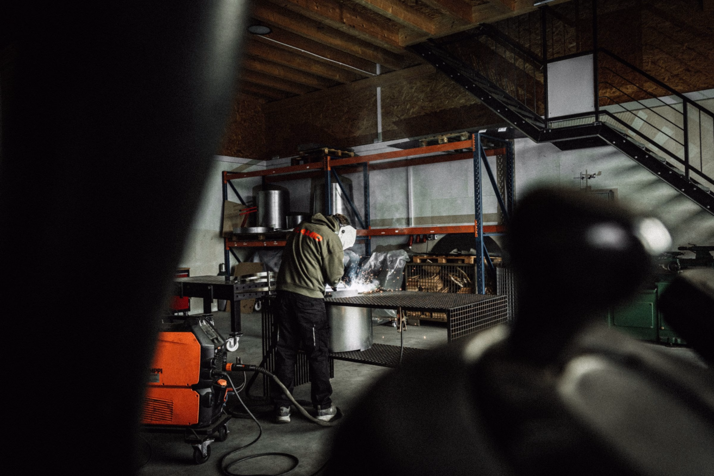 A welder in a workshop, creating steel grills for Flamid, sparks flying in a dimly lit industrial space.
