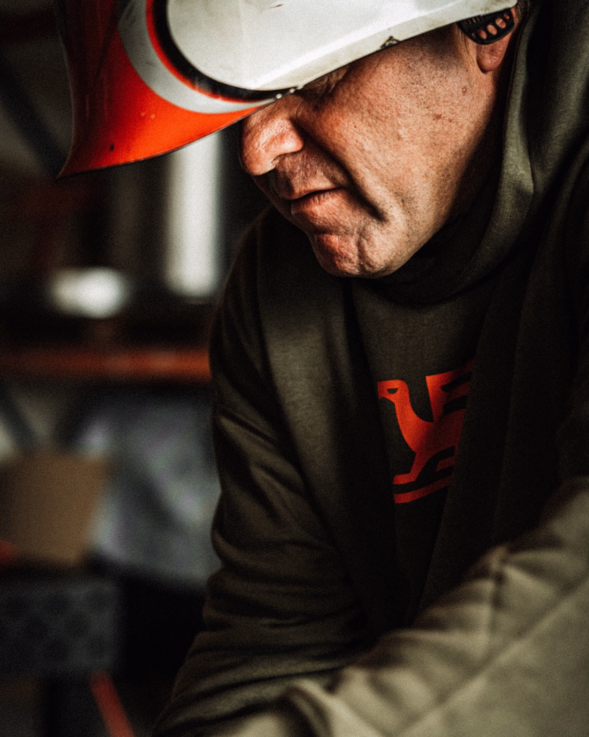 A man in a protective helmet leans forward, showcasing a red bird-in-the-F logo on his dark green sweatshirt.