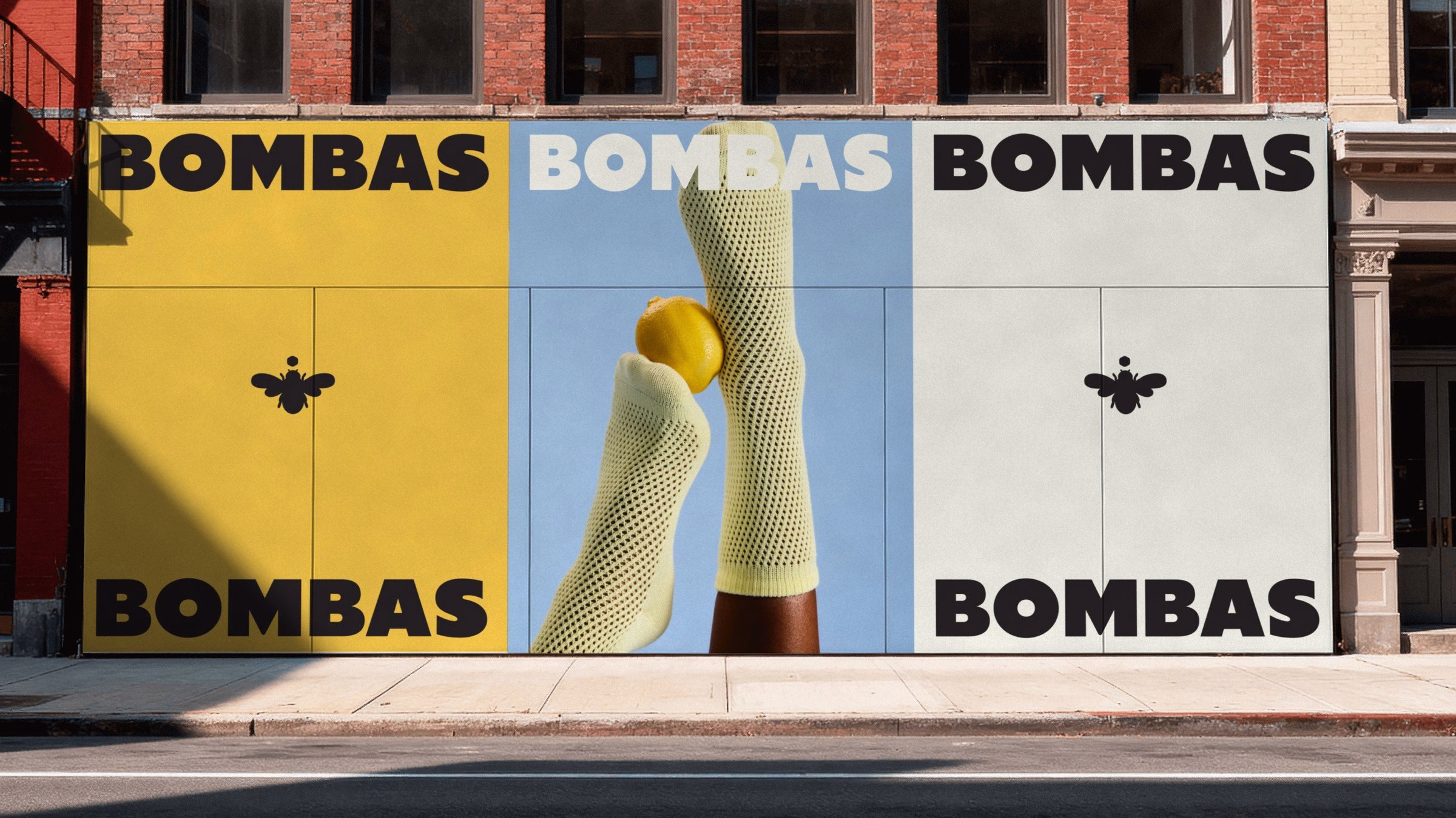A wall mural features oversized "Bombas" text, yellow and blue backgrounds, and mesh socks holding a lemon.
