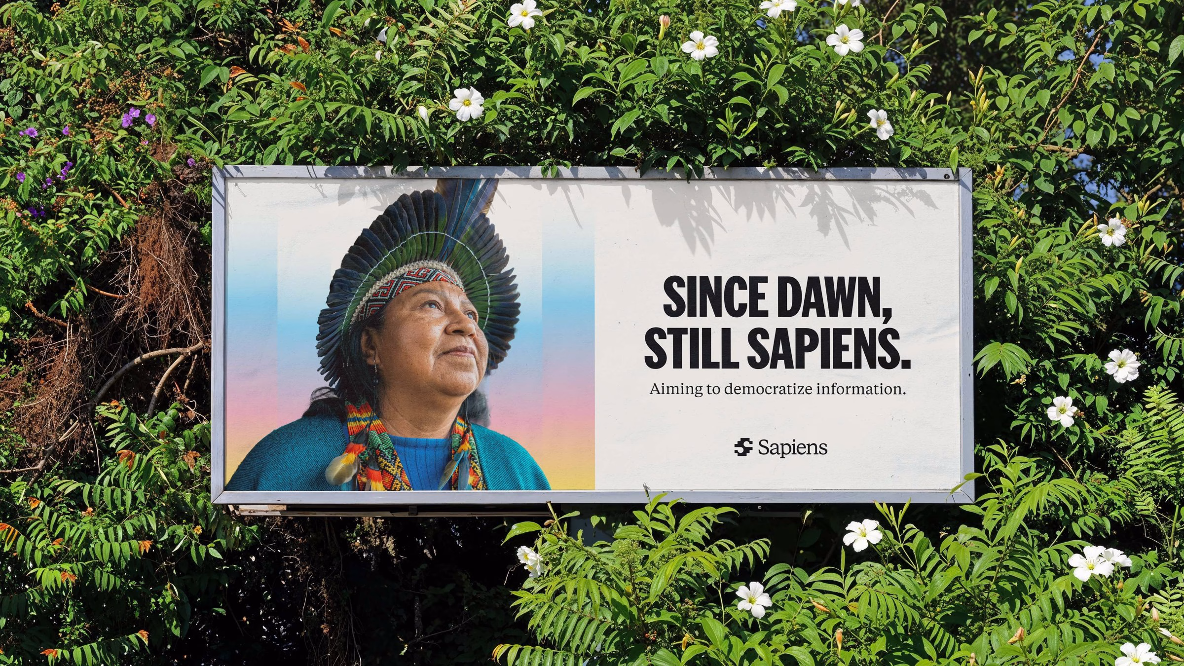 A billboard features a smiling Indigenous person in traditional attire, showcasing bold typography that reads "Since dawn, still Sapiens."