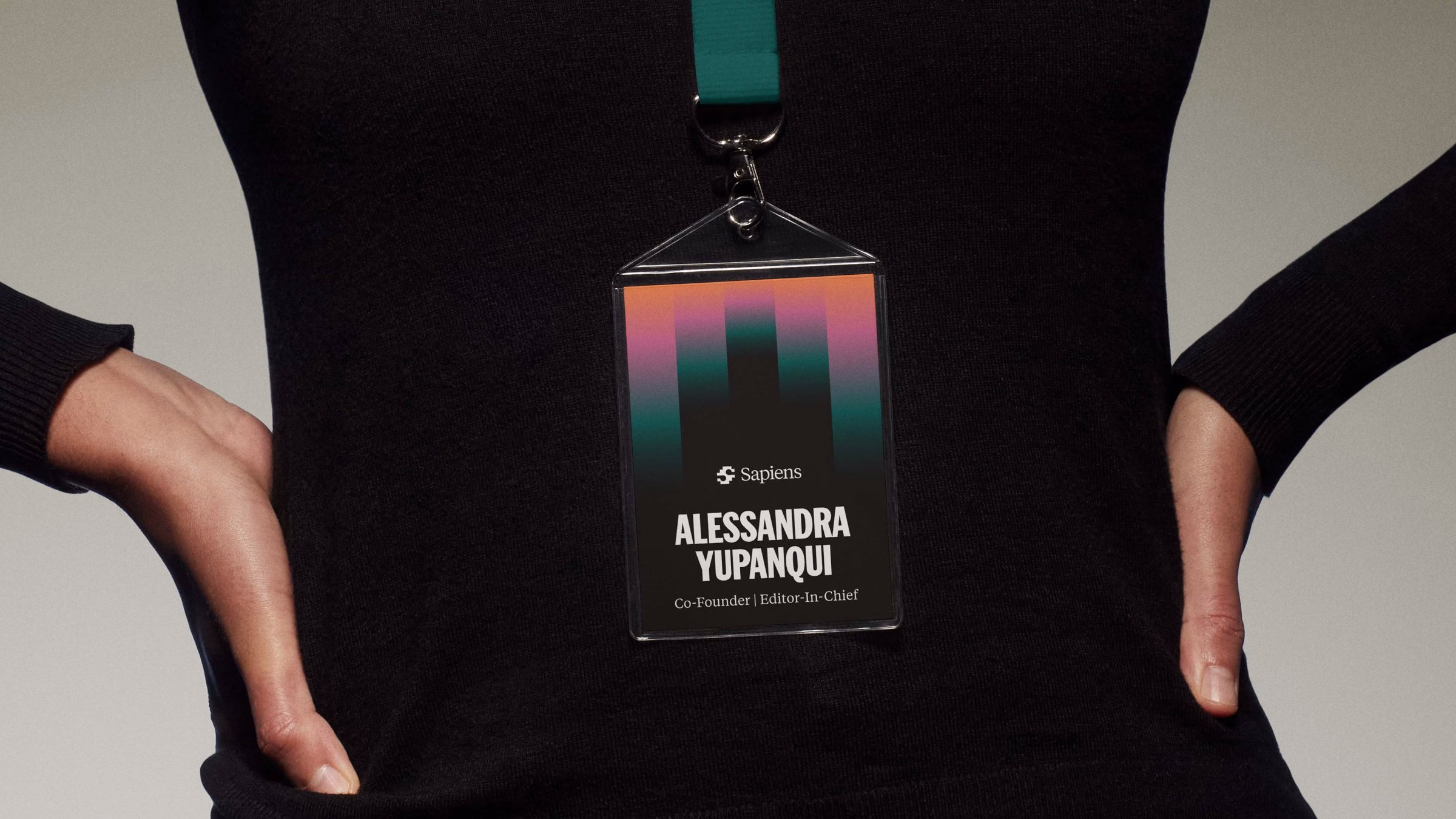 A close-up of a name badge with colorful gradient design, worn by a person in a black top, featuring the Sapiens logo.