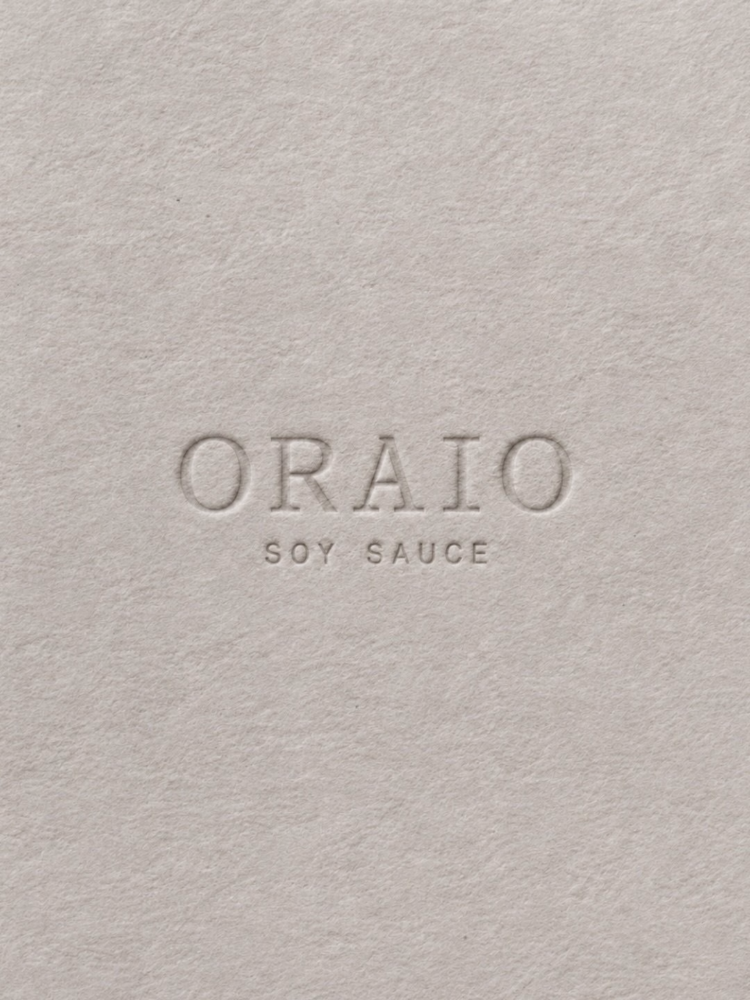 Embossed text reads "ORAIO SOY SAUCE" on a textured, neutral-colored paper background.