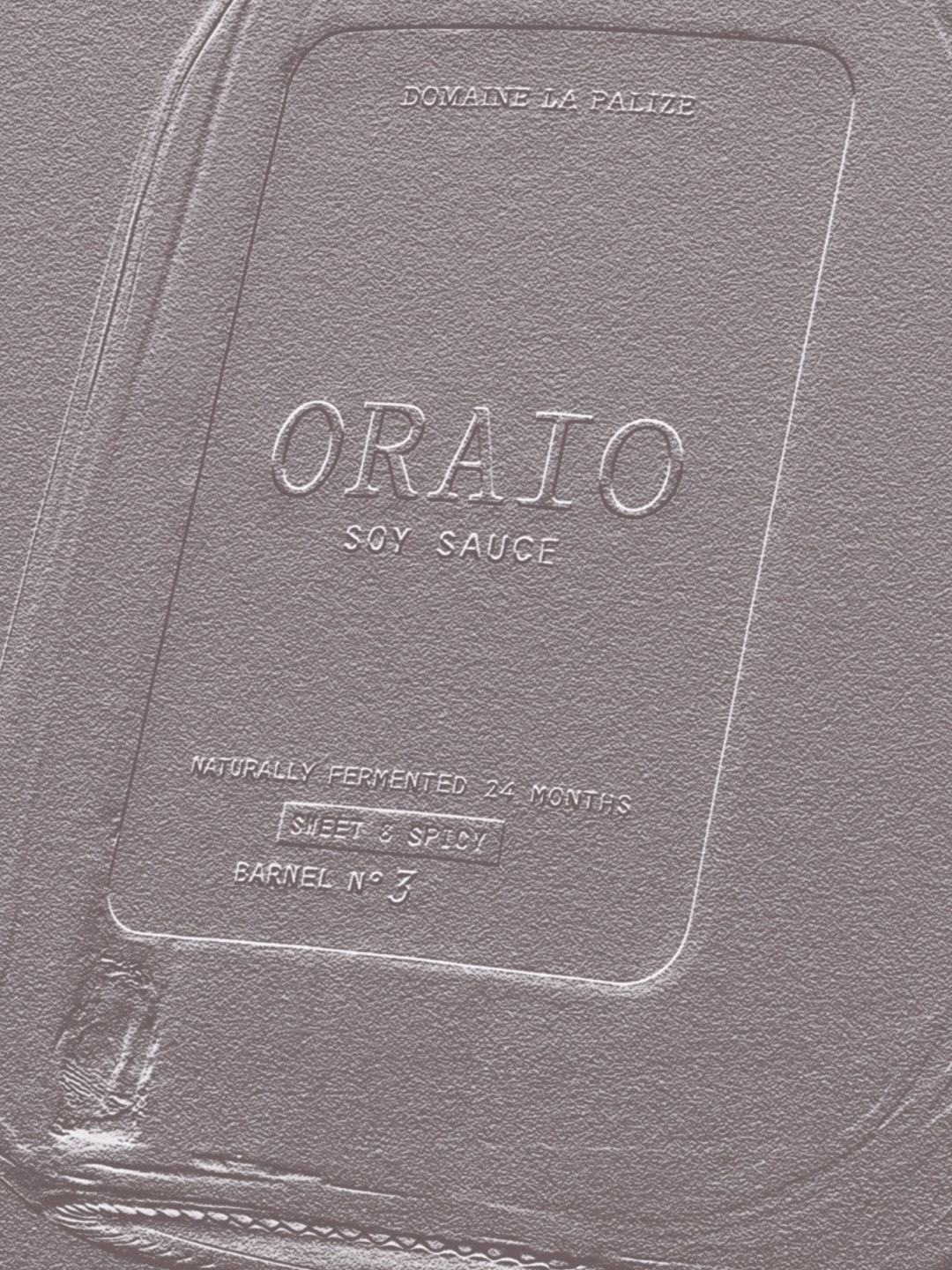 Embossed label on a light-hued soy sauce bottle features the name "Oraio" and detailing about fermentation.