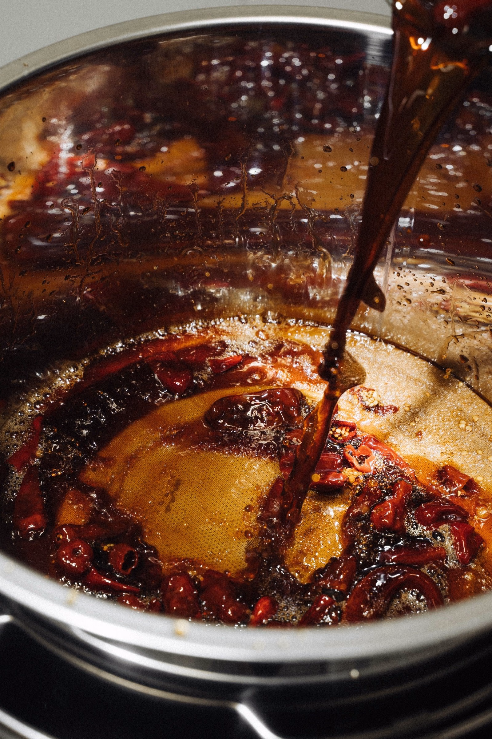 Dark soy sauce poured into a pot of cooked chillies for Oraio Sweet & Spicy