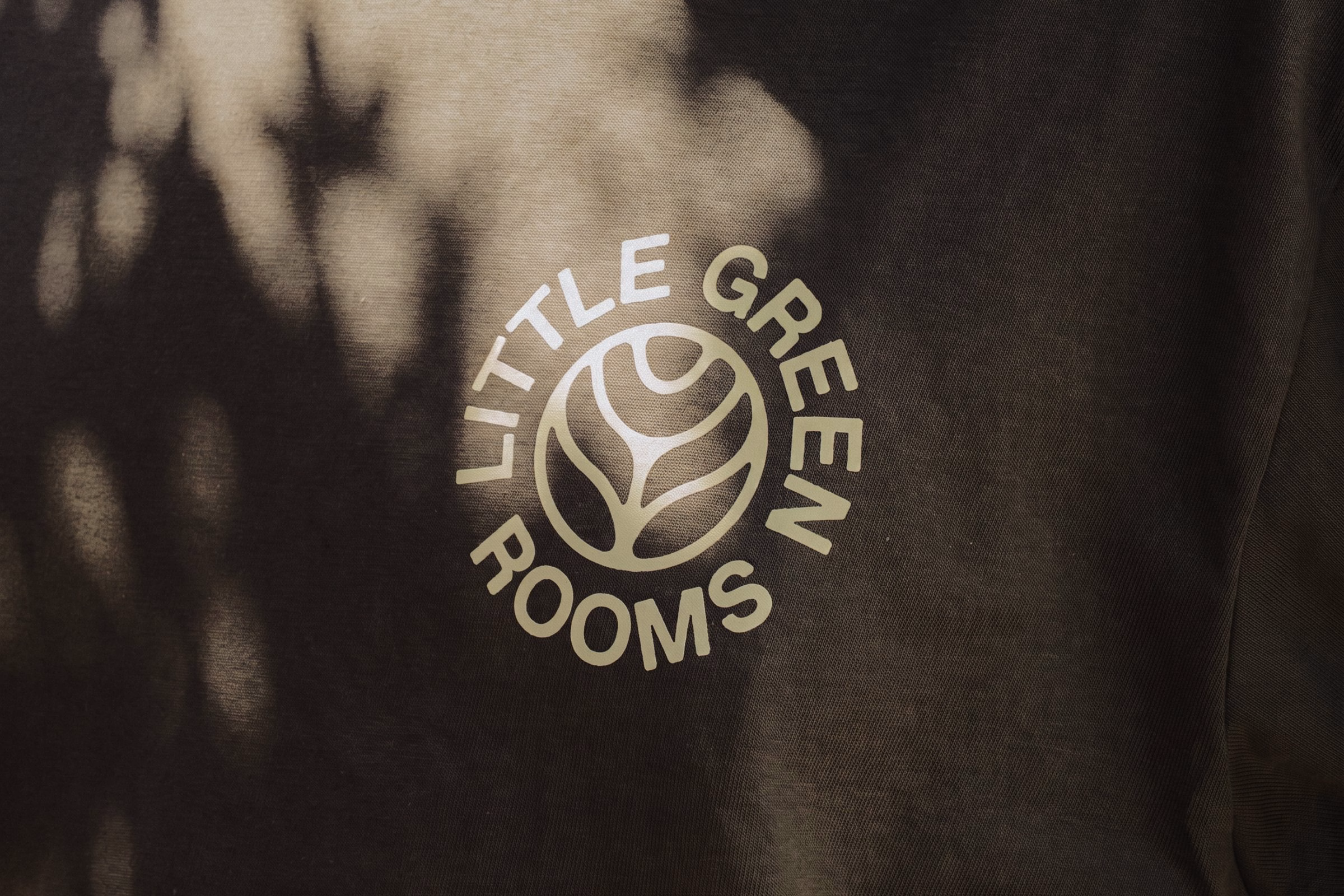 The logo for Little Green Rooms, featuring earthy tones and a circular design, rests on a textured background.