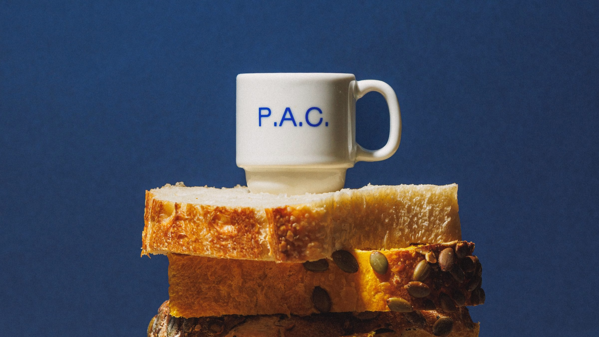 A white mug with blue text "P.A.C." sits atop slices of bread against a dark blue background.