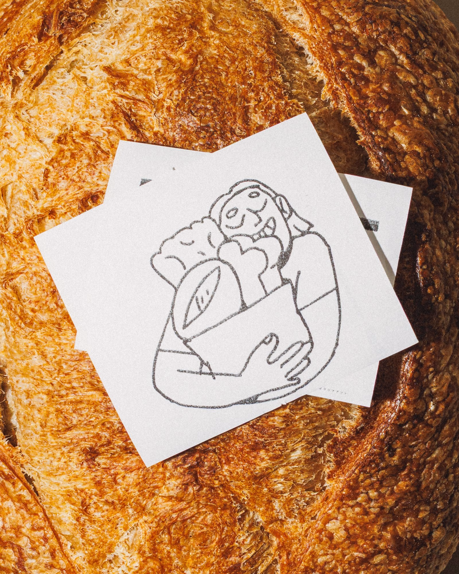 A textured loaf of bread serves as a backdrop for illustrated recipe cards depicting a person happily holding baked goods.