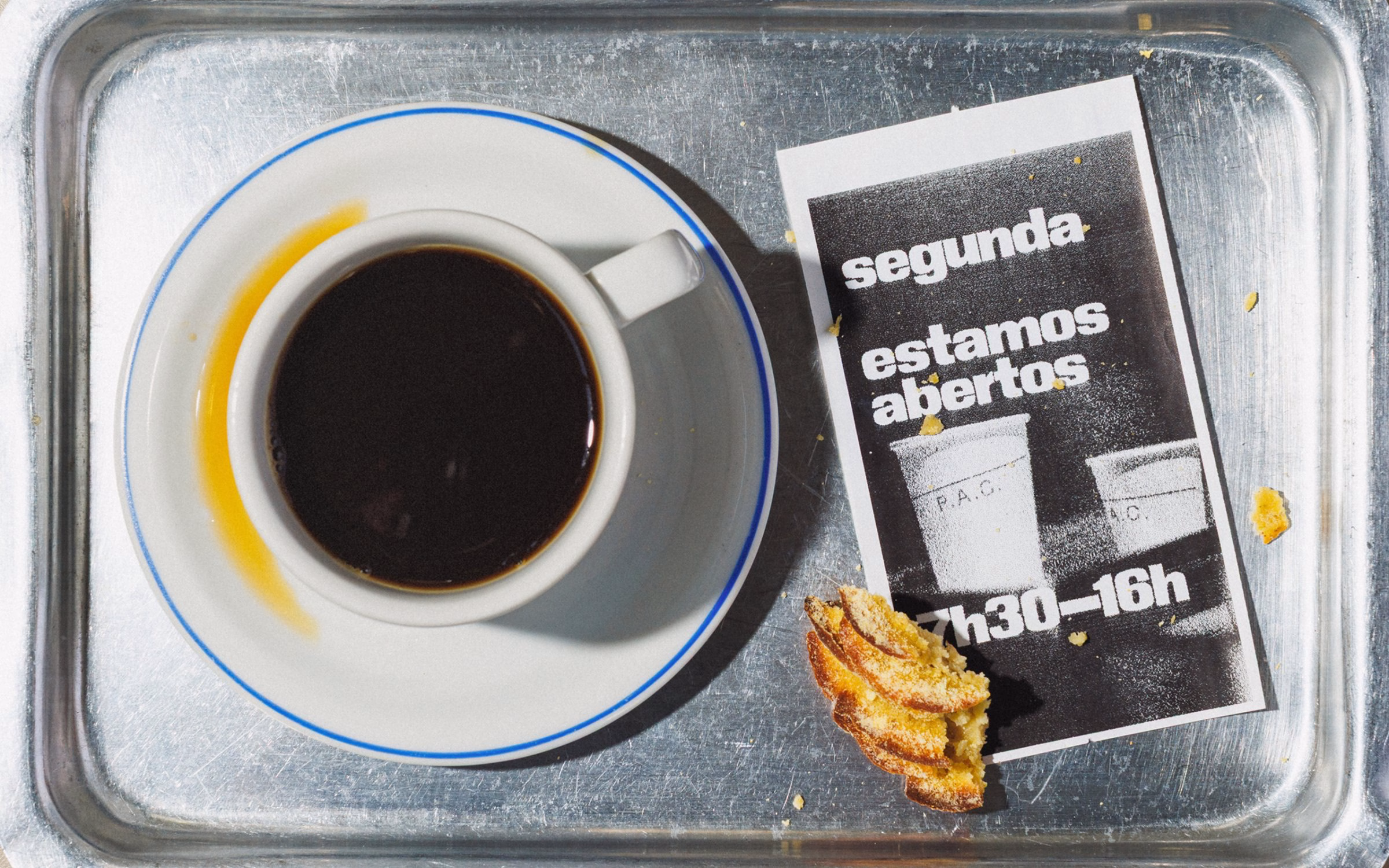 A silver tray holds a coffee cup, a receipt featuring bold typography, and a piece of cake with a golden crust.