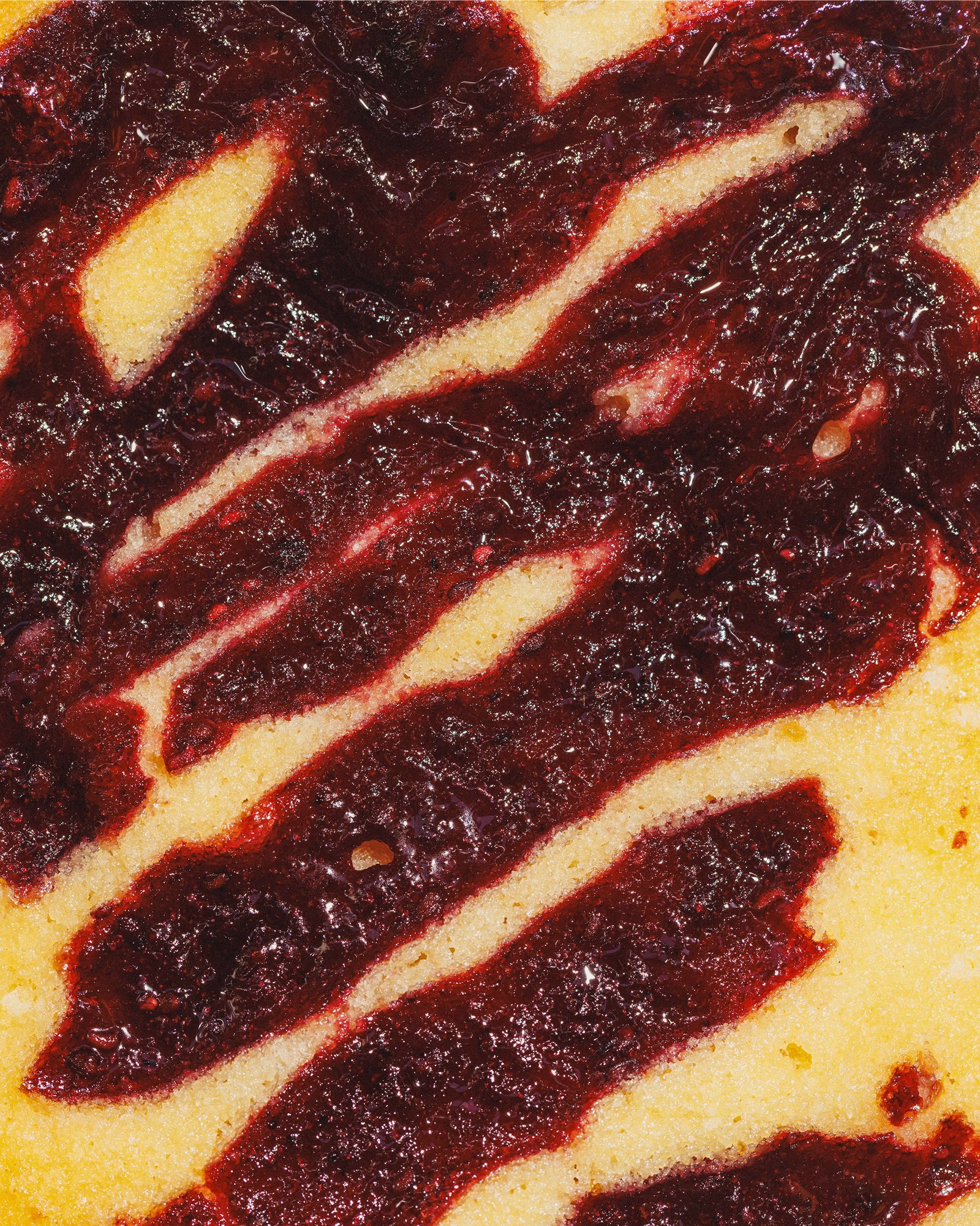 A close-up of a bakery item with a swirl of dark red jam on a pale yellow cake, showcasing the unique dessert design.