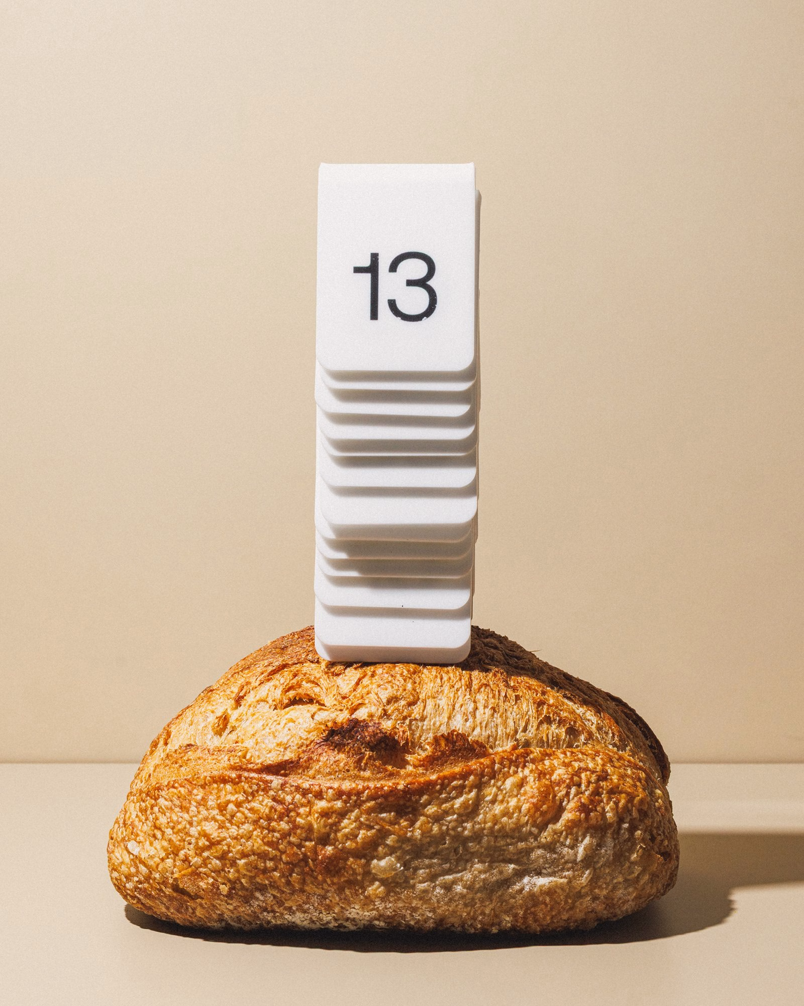 A textured loaf of bread sits beneath a stacked white receipt printer with the number 13 prominently displayed.
