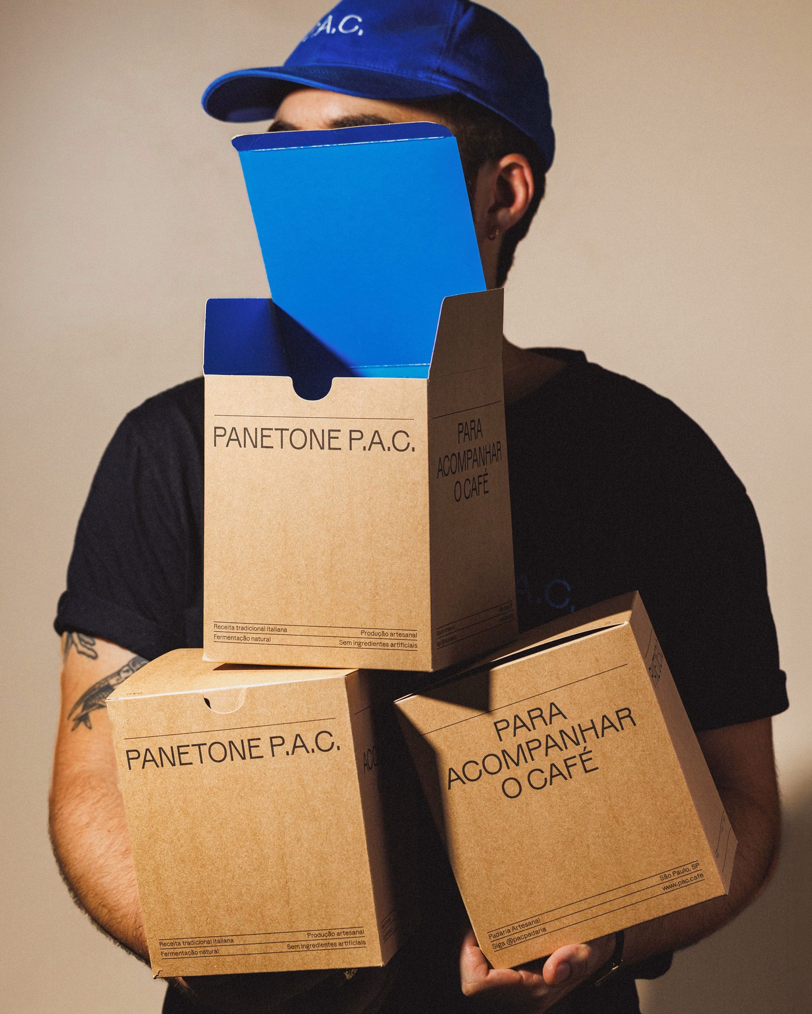 Person in a blue P.A.C. cap holding kraft panettone boxes