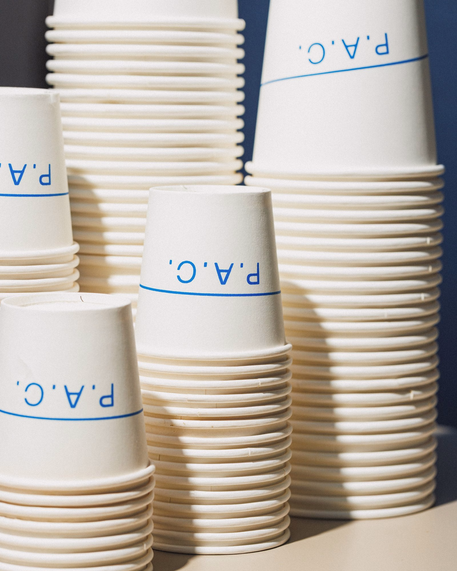 Stacks of white P.A.C. paper coffee cups with blue rim logo