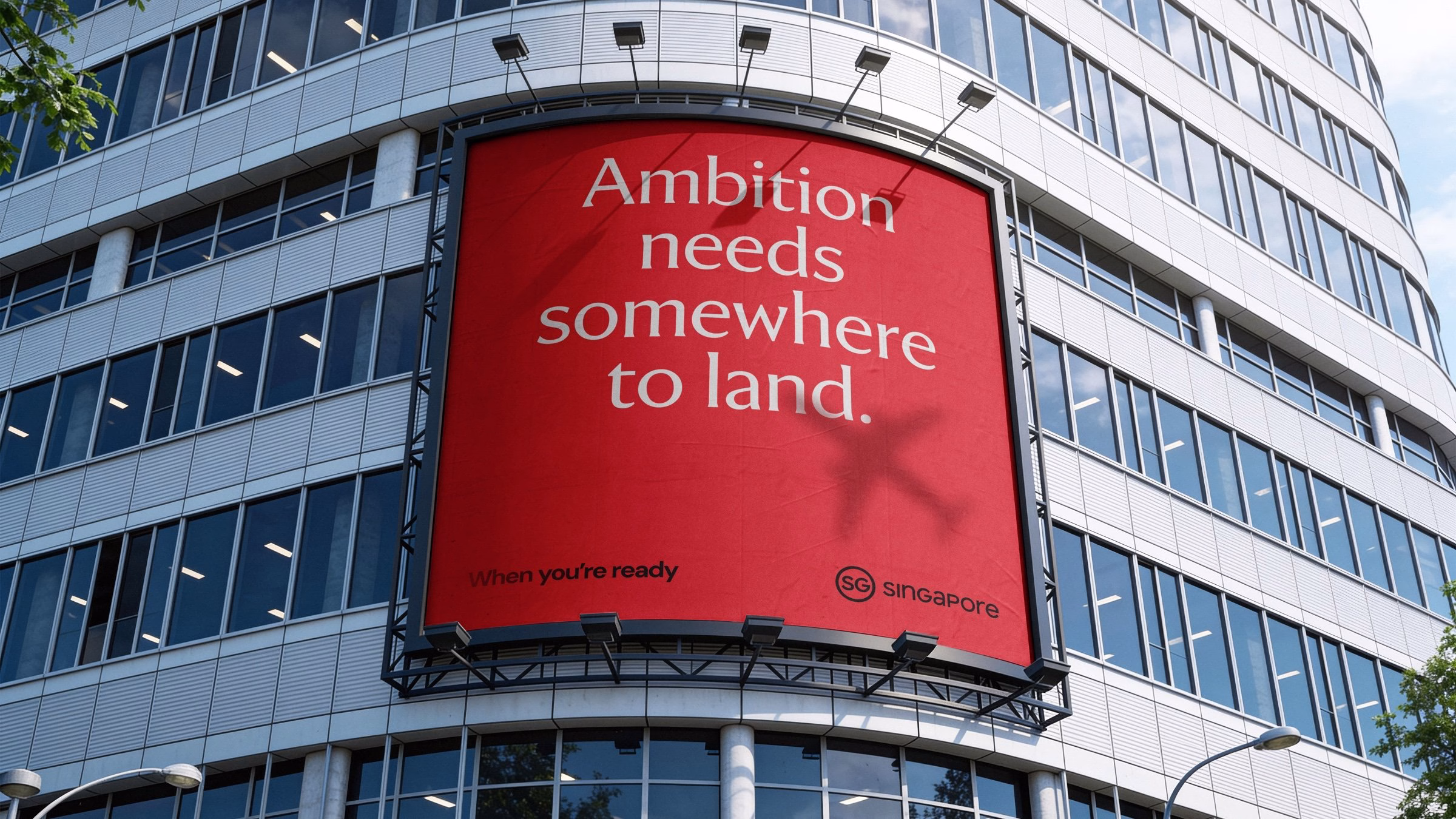 A large red billboard on a modern building features the phrase "Ambition needs somewhere to land" in white typography.