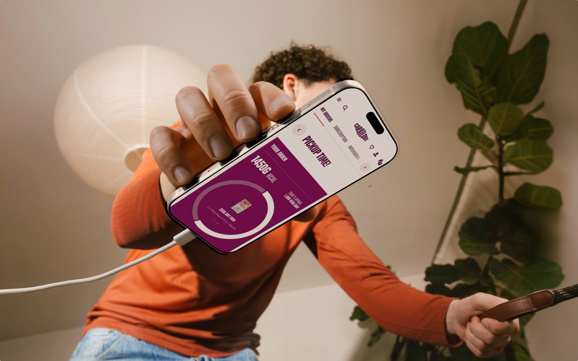 A hand holds a smartphone displaying a purple interface for Carnilove's pet food order in a bright indoor setting.