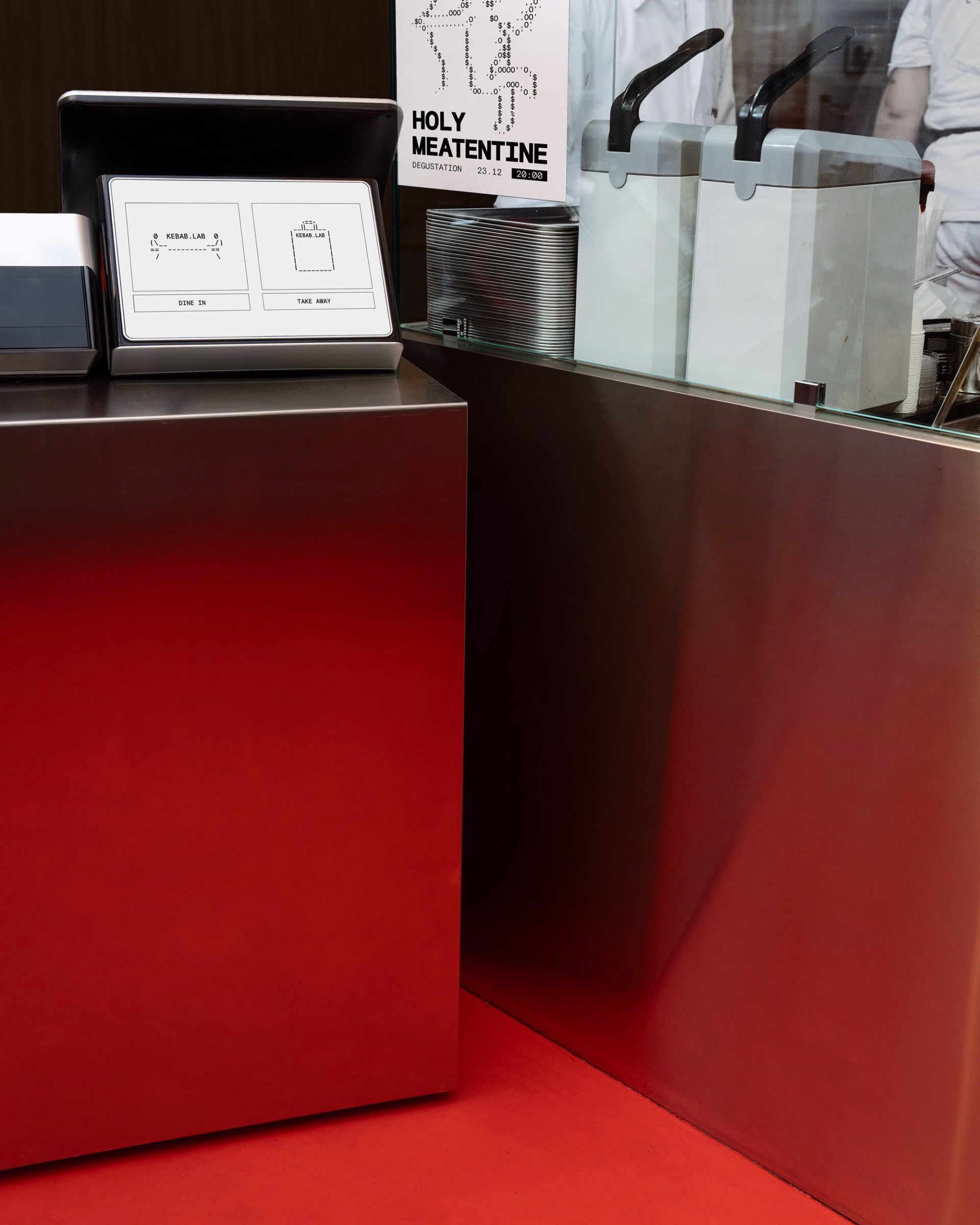 A sleek stainless-steel counter displays a digital menu for Kebab.Lab, complemented by a bold red floor.