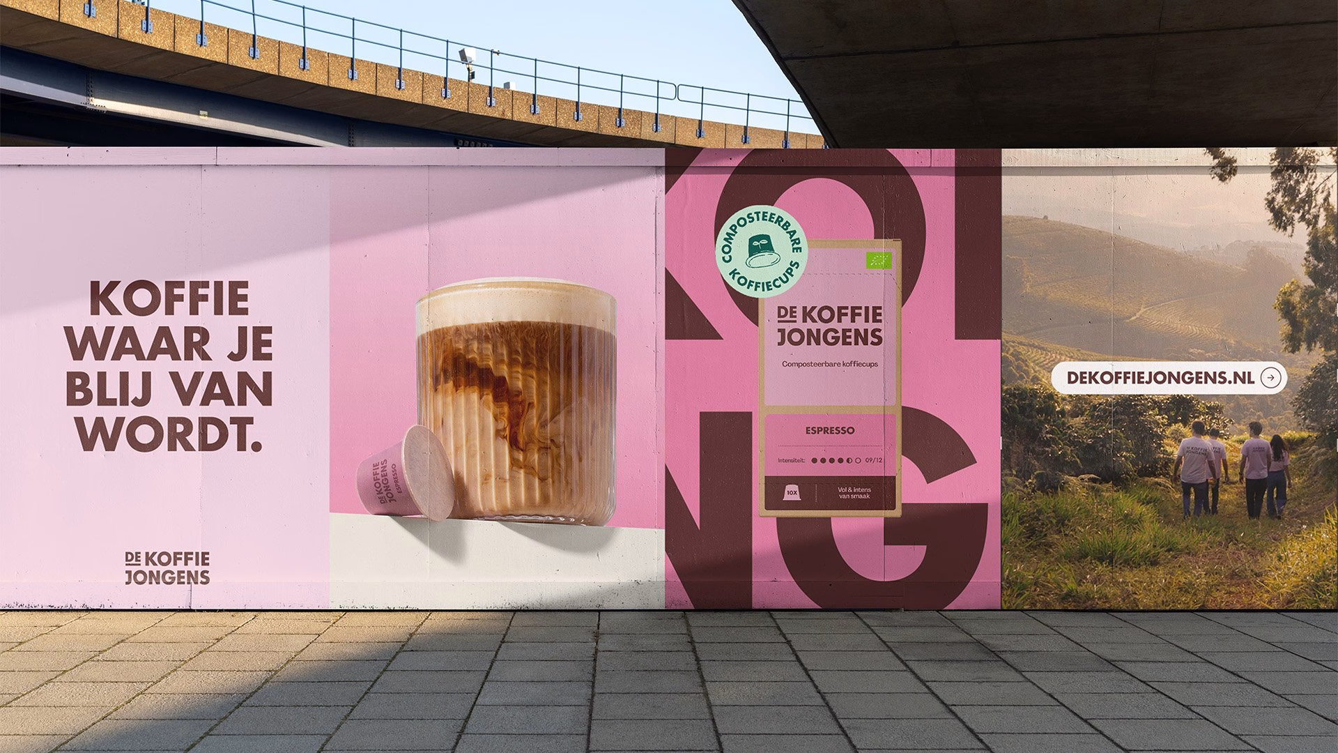 A vibrant pink wall displays De Koffiejongens branding, featuring coffee packaging and a scenic background.