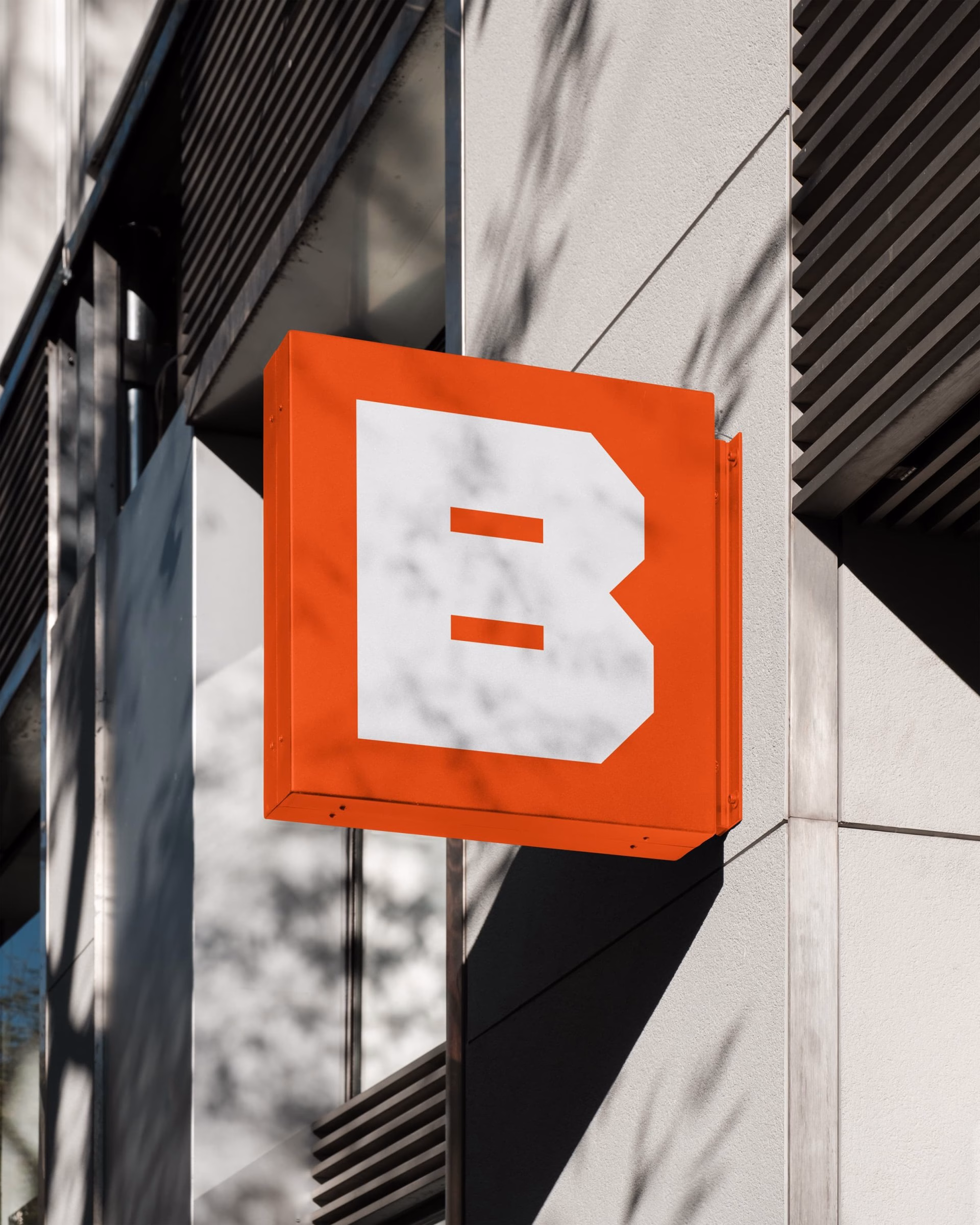 An orange sign featuring a bold white 'B' hangs on a modern building, showcasing brand identity and typography design.