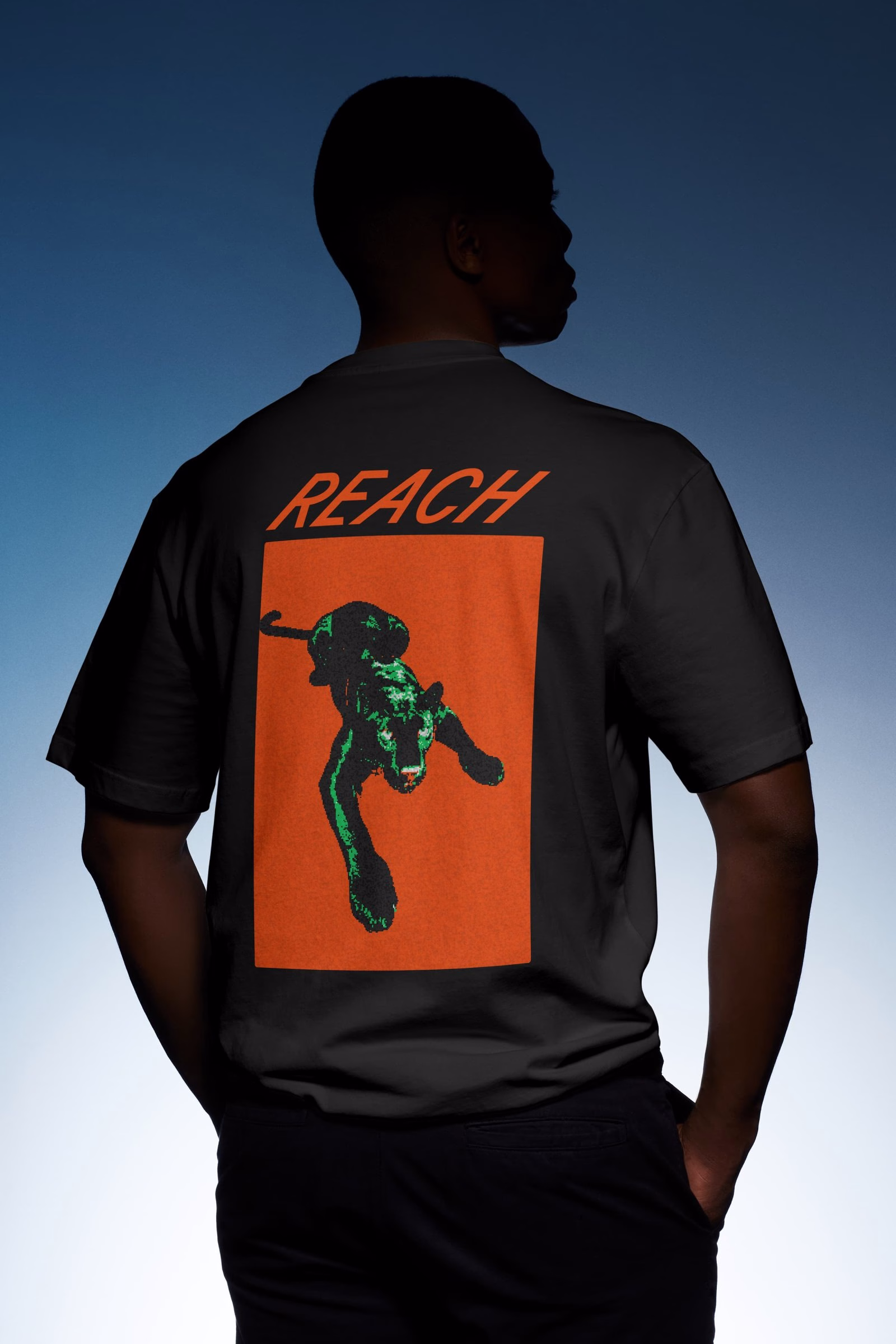 A person wearing a black t-shirt with a vivid green panther design and the word "REACH" on an orange background.