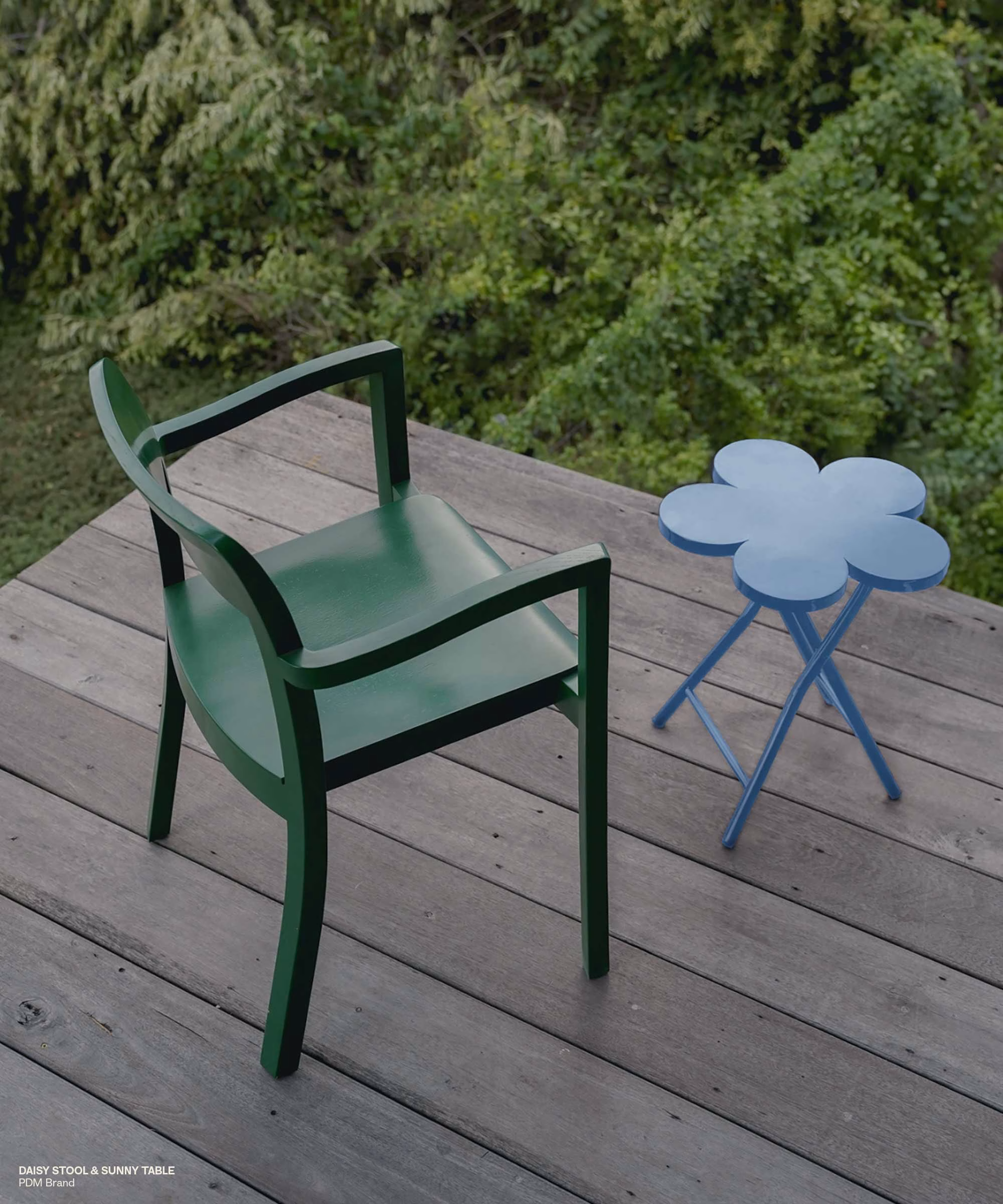 A lichen green chair and blue flower-shaped table sit on a wooden deck overlooking lush greenery, reflecting modern design.