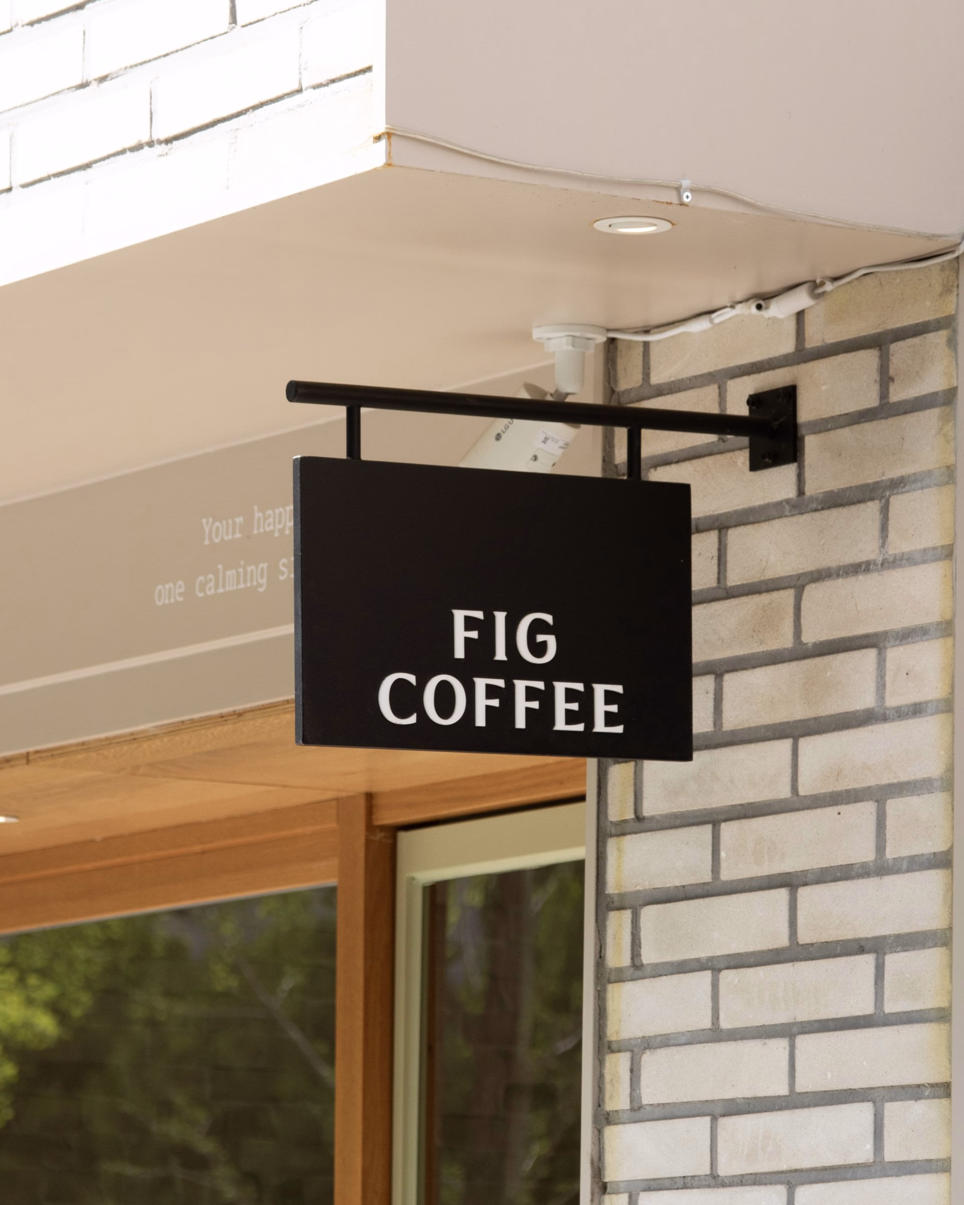 Signage for Fig Coffee features bold white typography on a black background, mounted beside a brick facade.