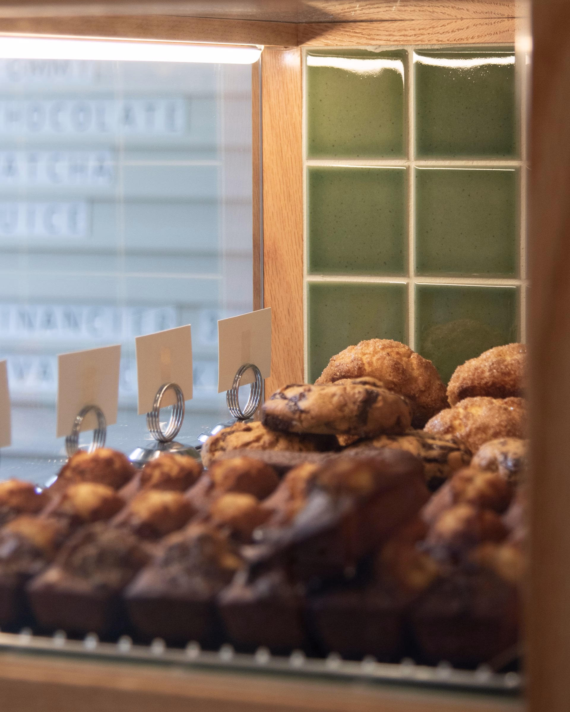 Pastries are displayed behind a glass case, with a green tiled background adding to the cafe's inviting brand identity.