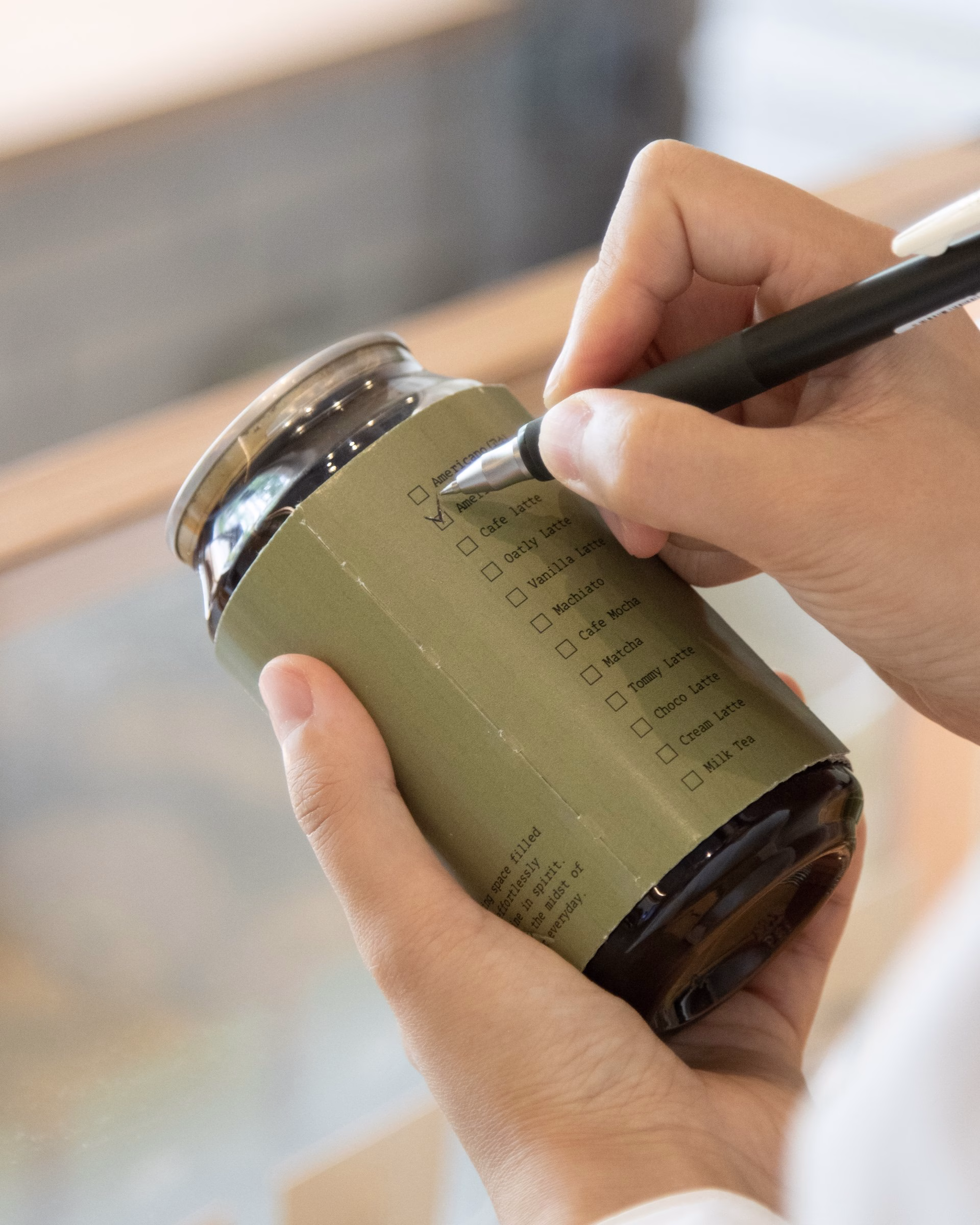 A hand holds a glass jar wrapped in a green label with a checklist for coffee drinks from Fig Coffee.