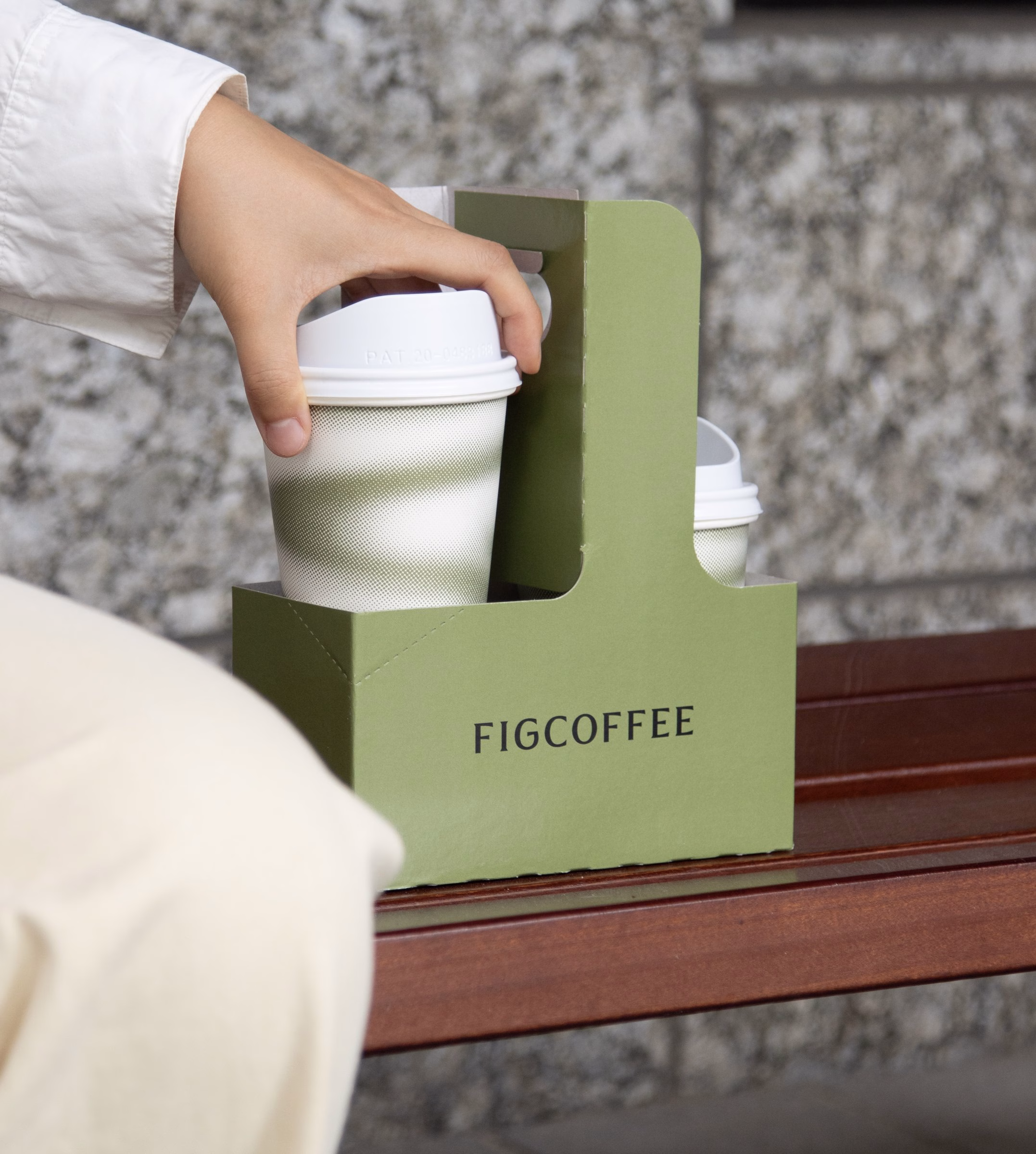 A hand reaches for coffee cups in a green holder, featuring the brand name Fig Coffee in sleek typography.