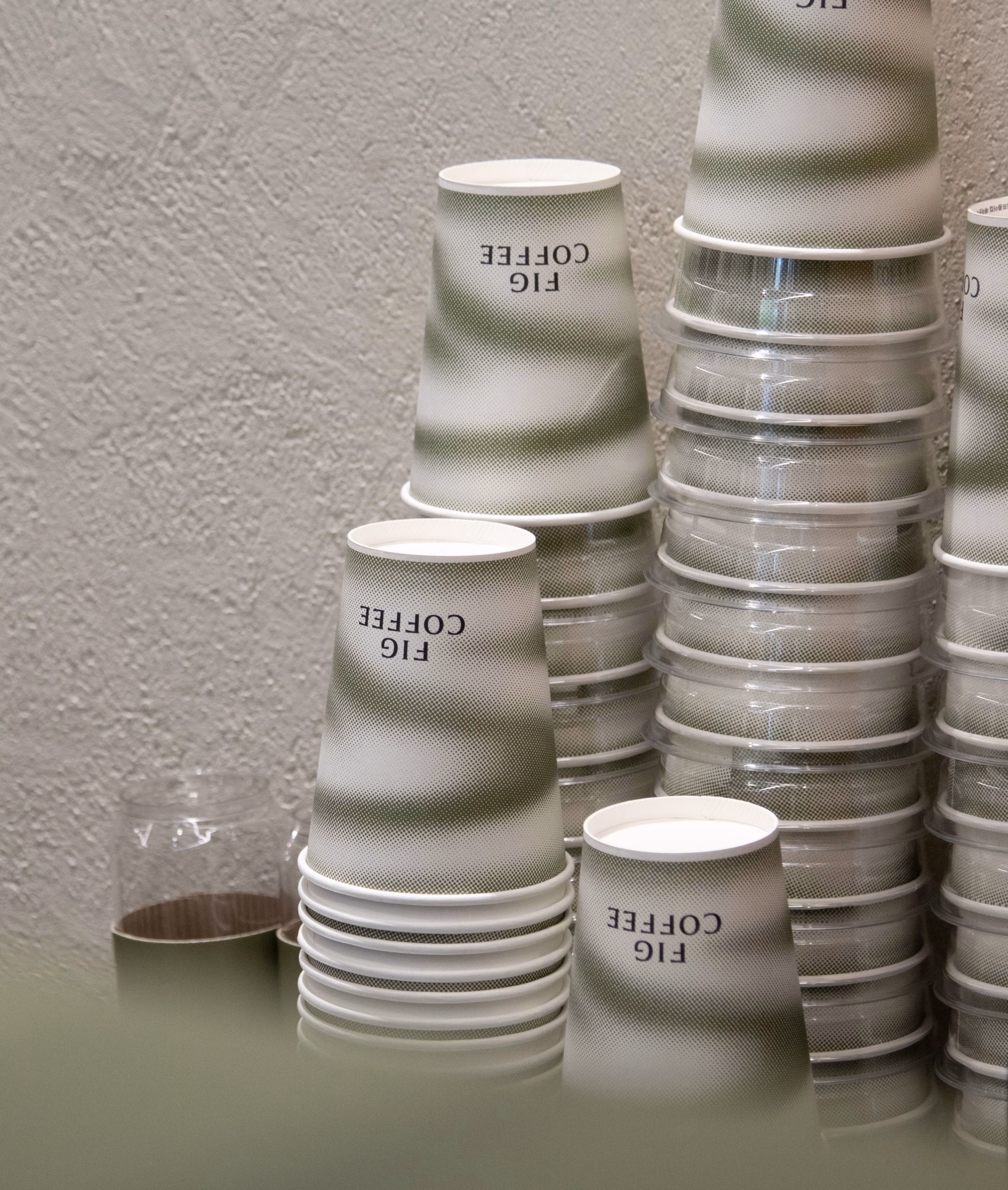 Stack of Fig Coffee paper cups with green gradient bands, cafe packaging
