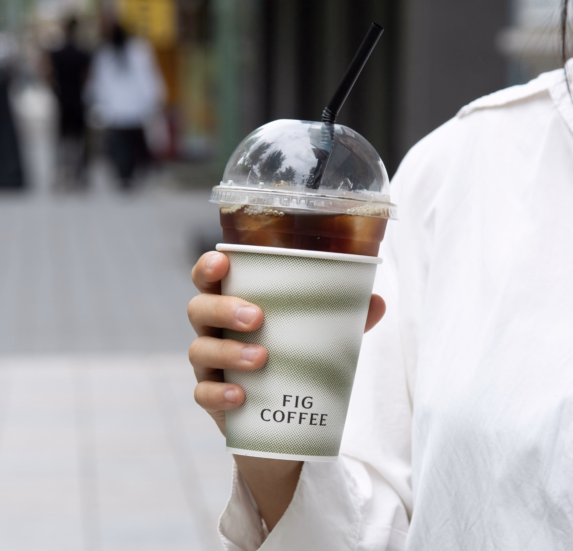 Iced coffee in a clear Fig Coffee cup held on a Seoul street