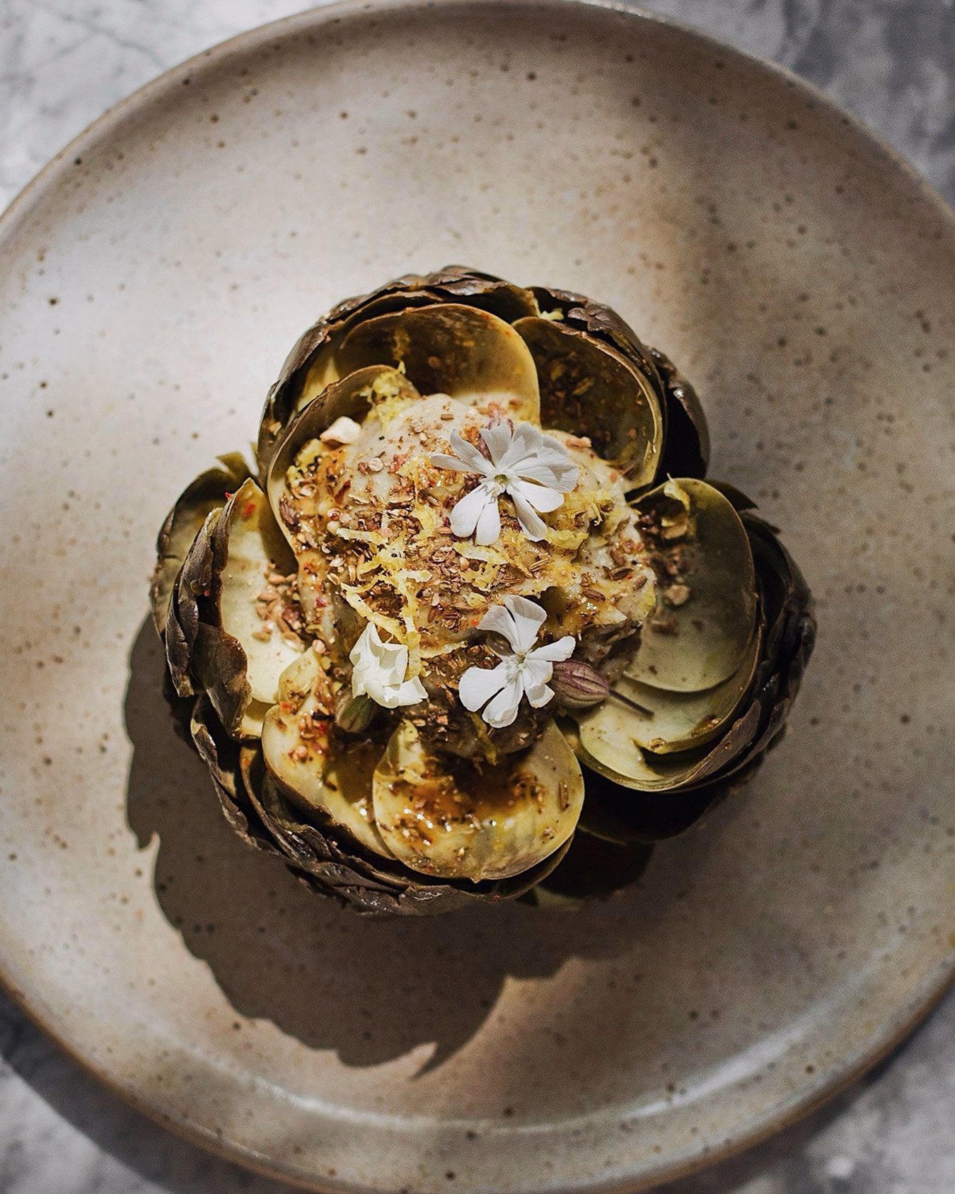 An artfully arranged dish with layered leaves, garnished with edible flowers, on a textured beige plate.