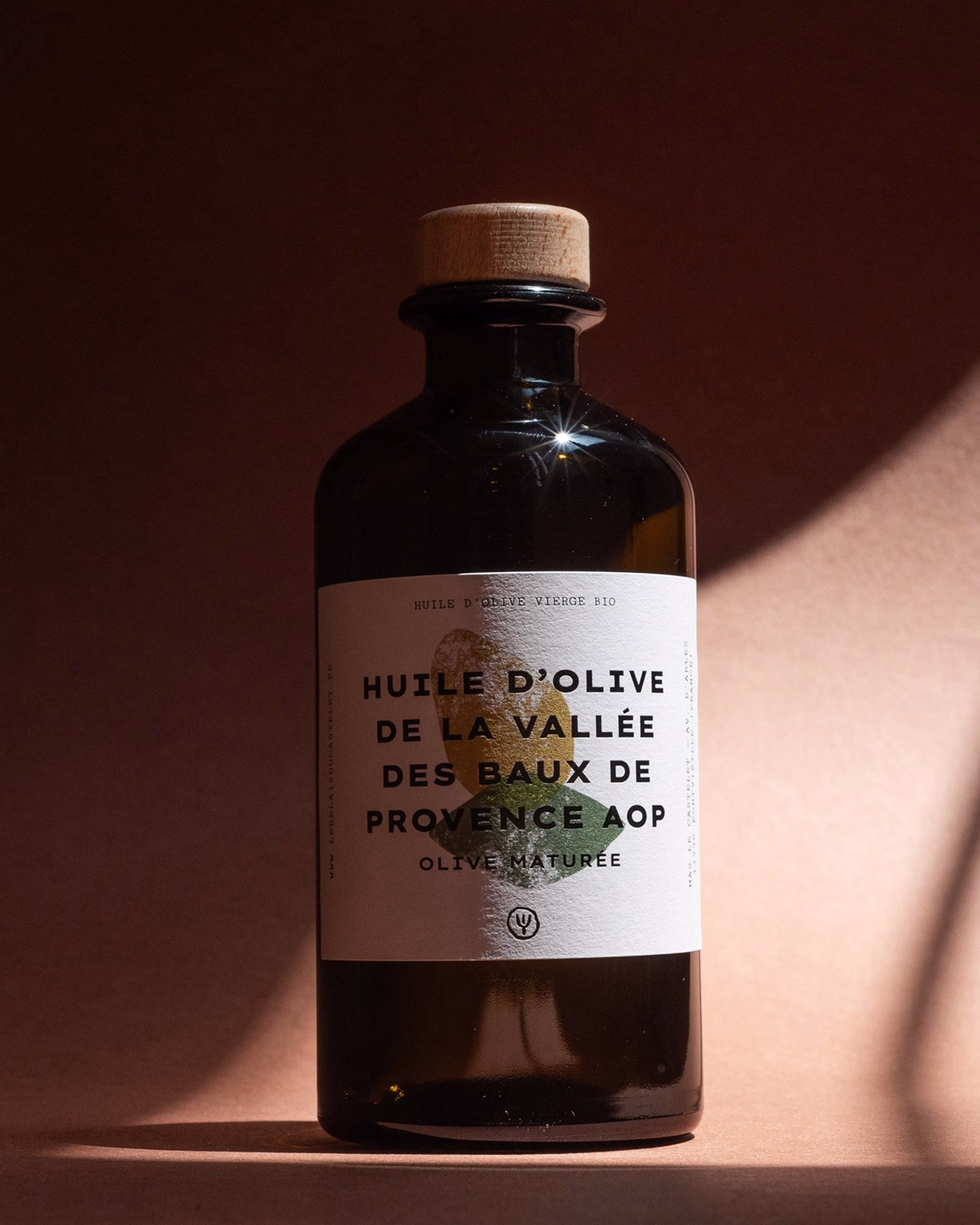 A dark glass bottle with a cork, featuring a textured white label displaying hand-drawn typography against a warm background.