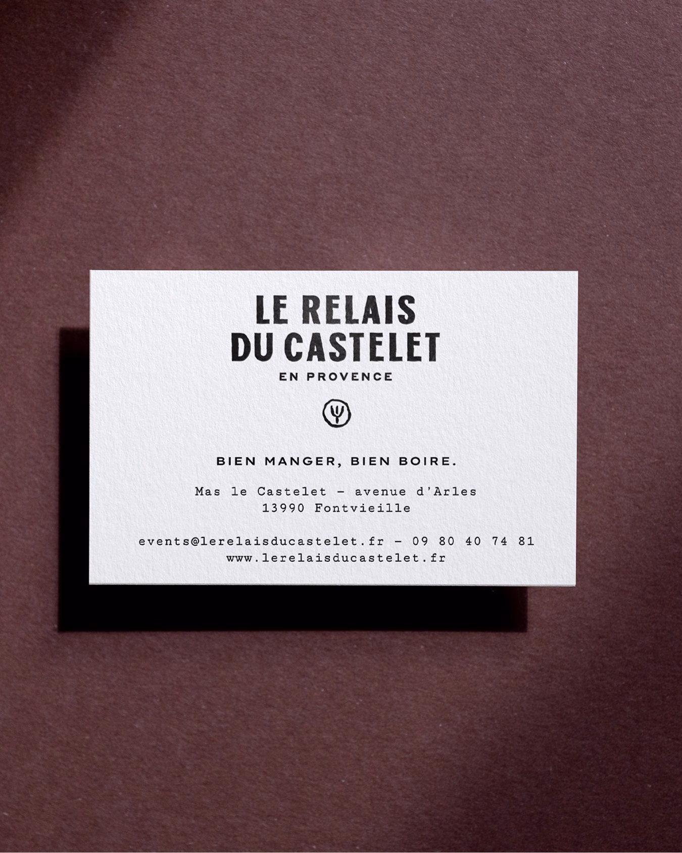 A textured white business card featuring bold black typography for Le Relais du Castelet against a dark brown background.